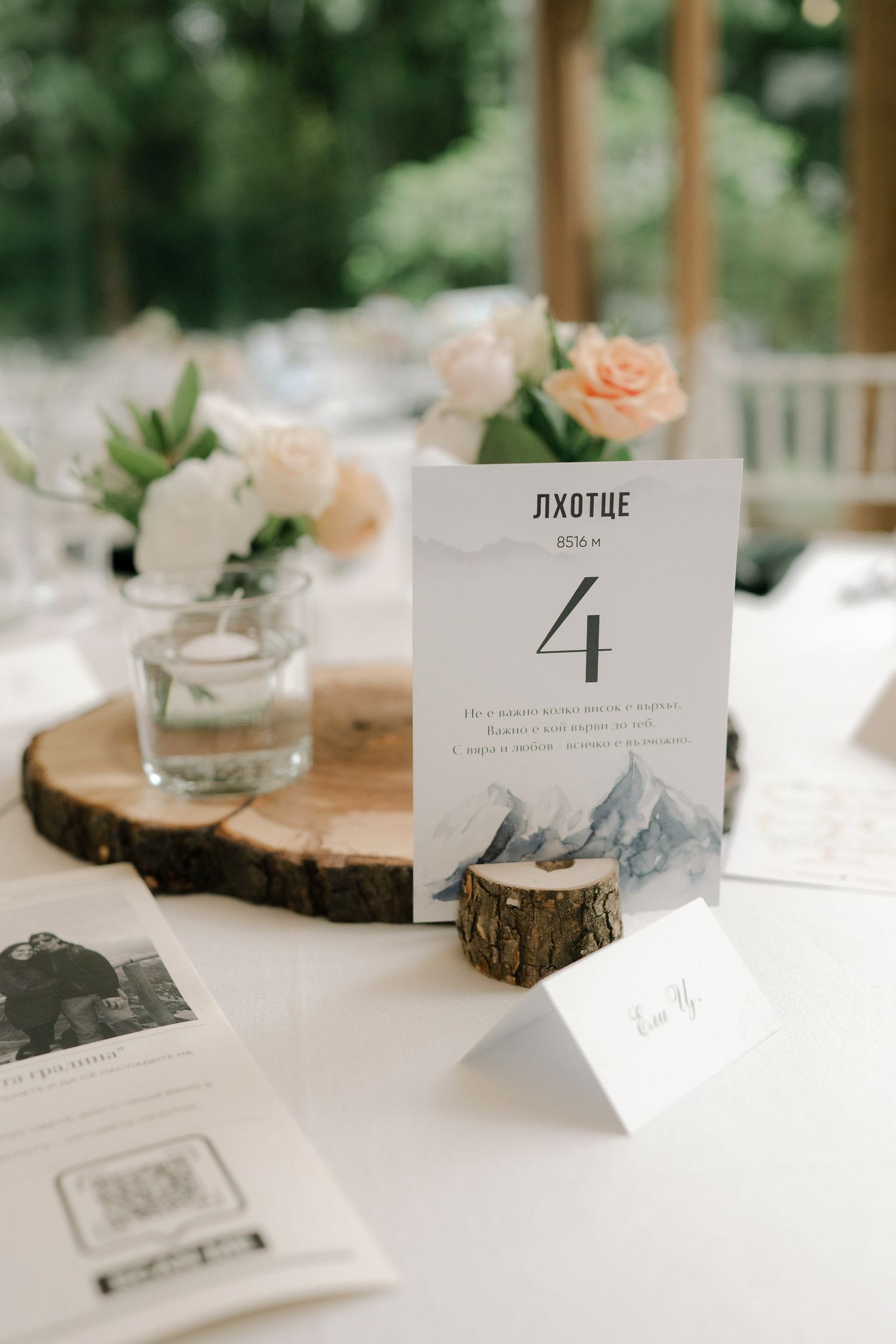 Rustic wedding table setting with wood slice centerpieces, peach roses, and elegant table number cards on white linens.