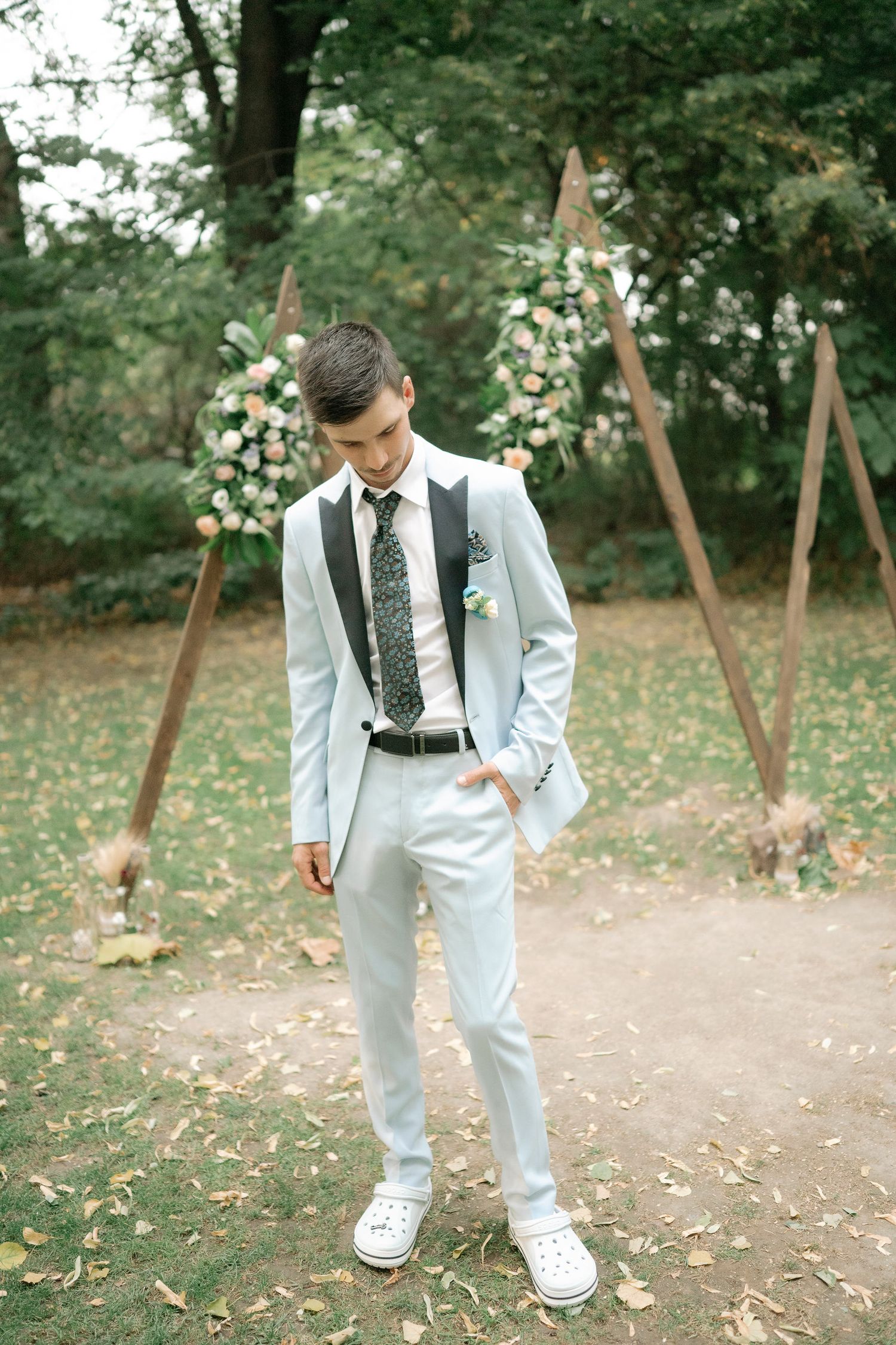 White dress shoes on a path scattered with flower petals in a garden setting.