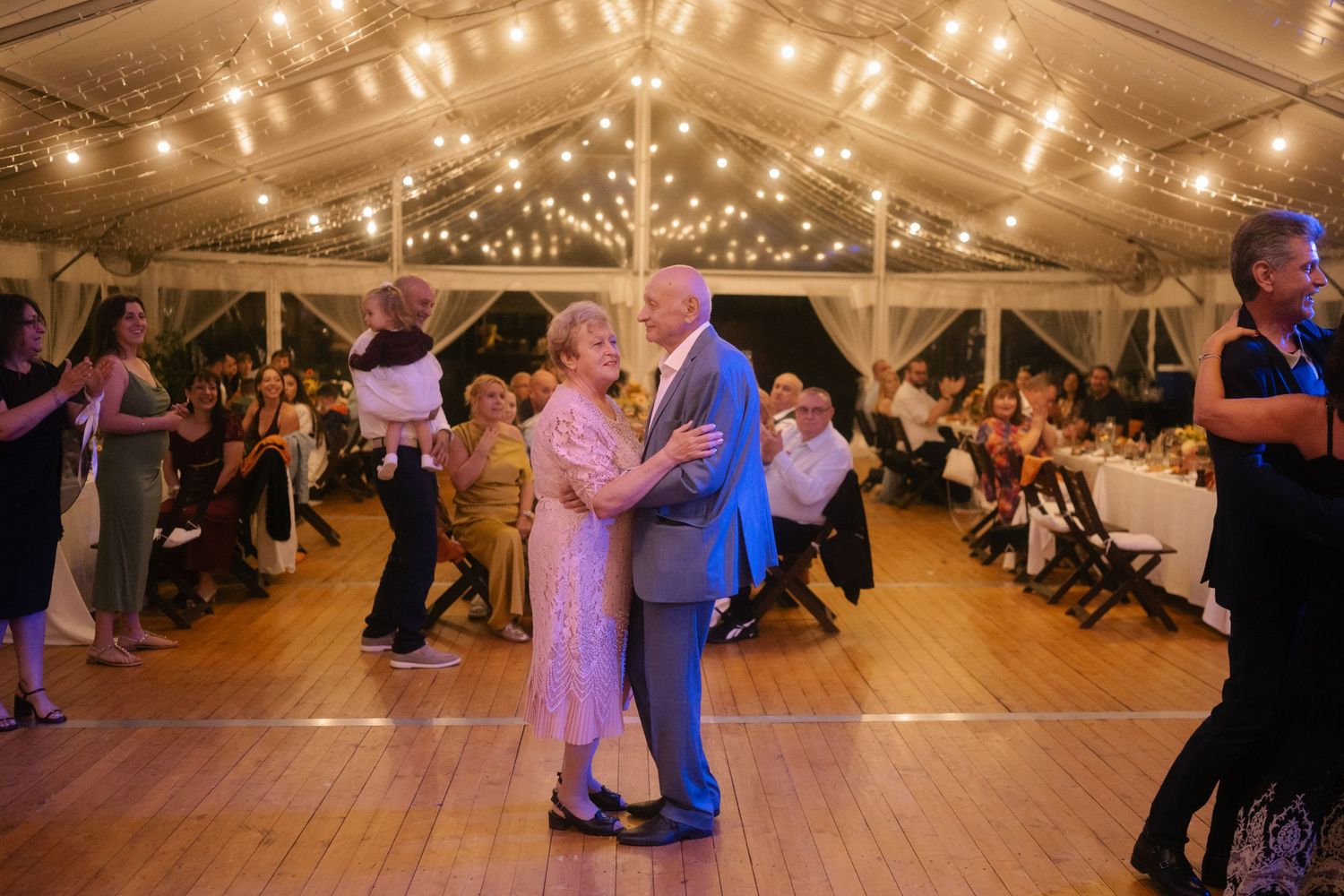 Large indoor wedding venue with string lights and purple accent lighting creating an elegant dance floor atmosphere.
