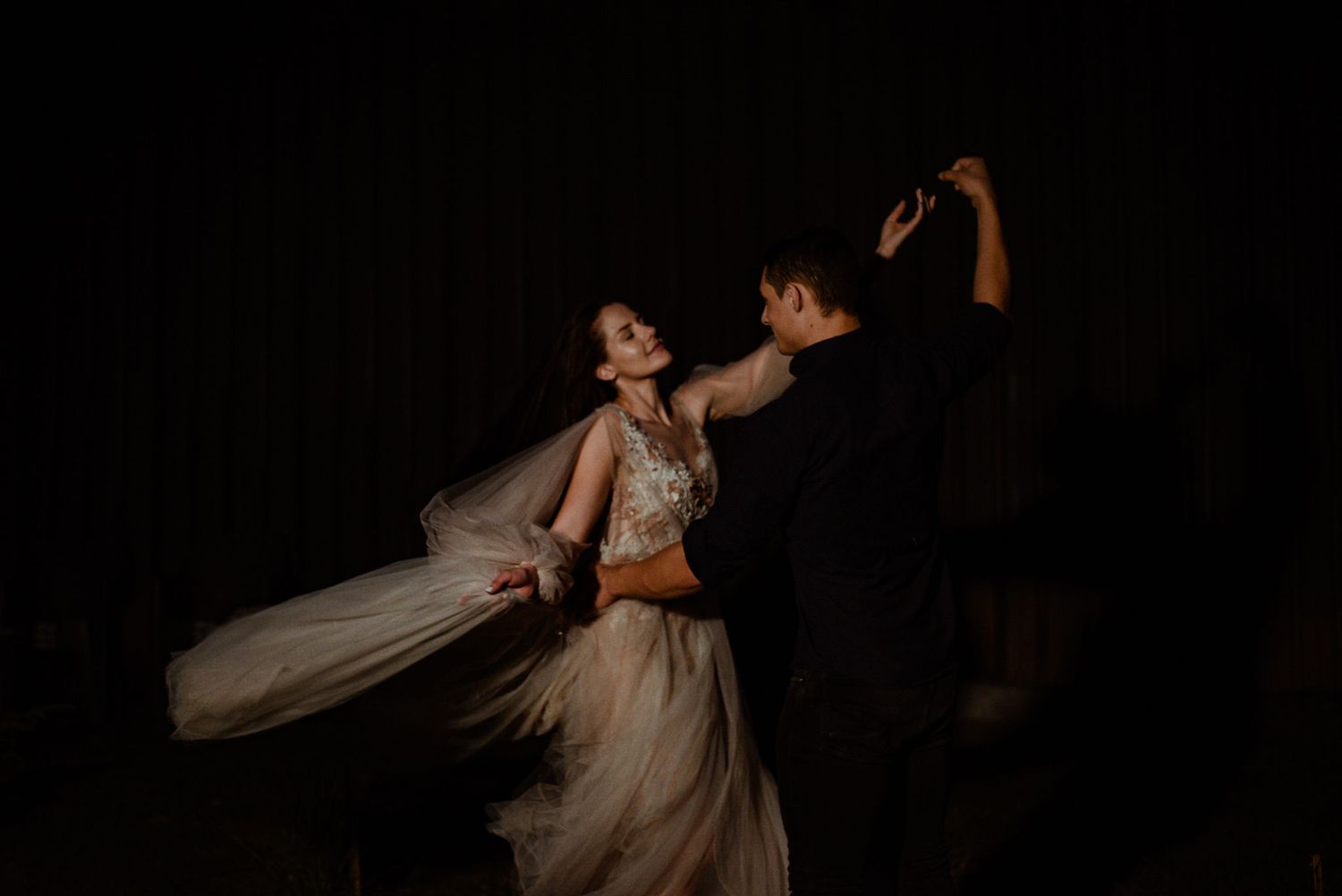 A bride and groom share an intimate dance together at their wedding reception on a dark dance floor.
