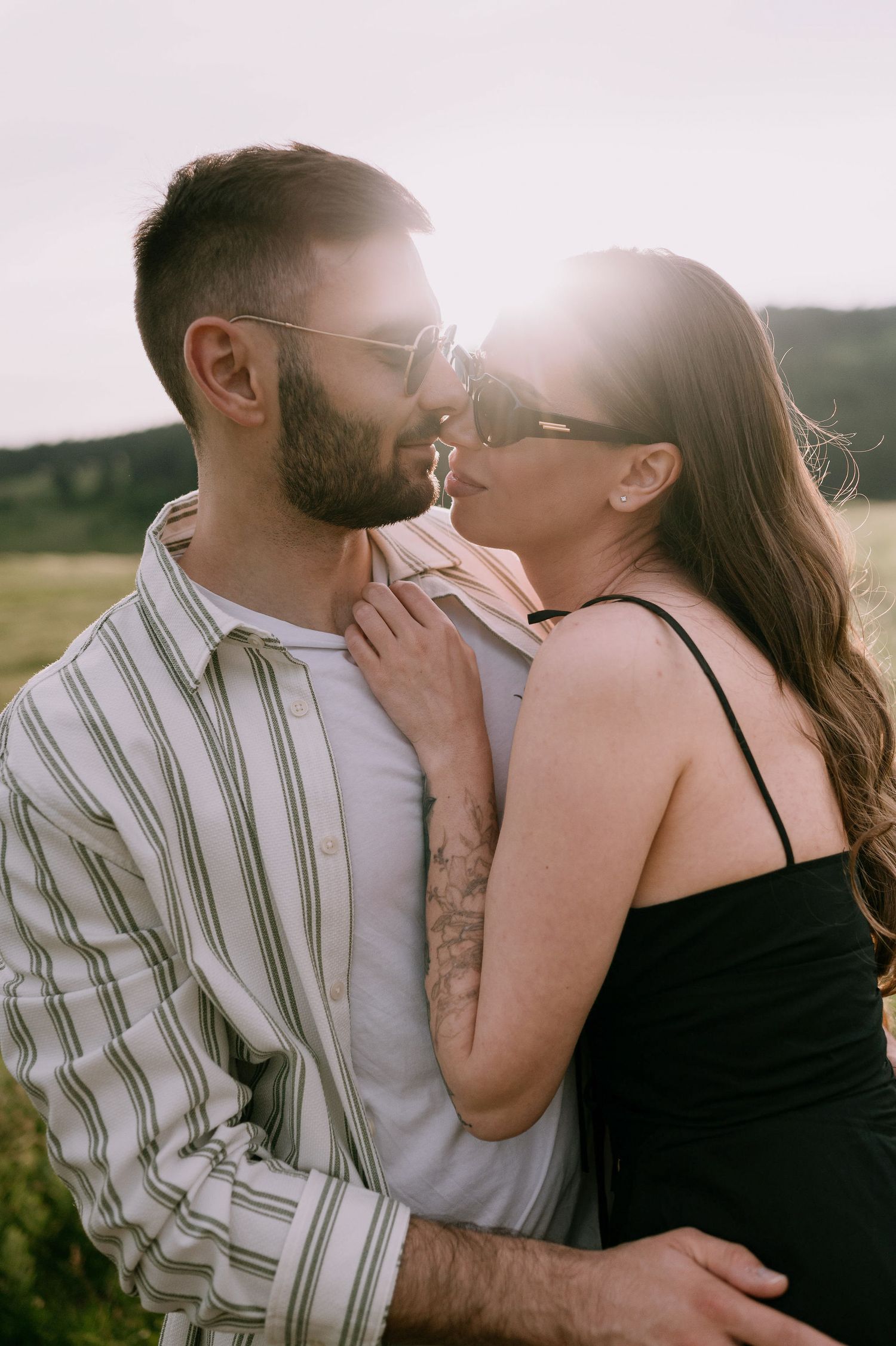 A romantic couple embraces in a sunlit field during golden hour, sharing an intimate moment together.