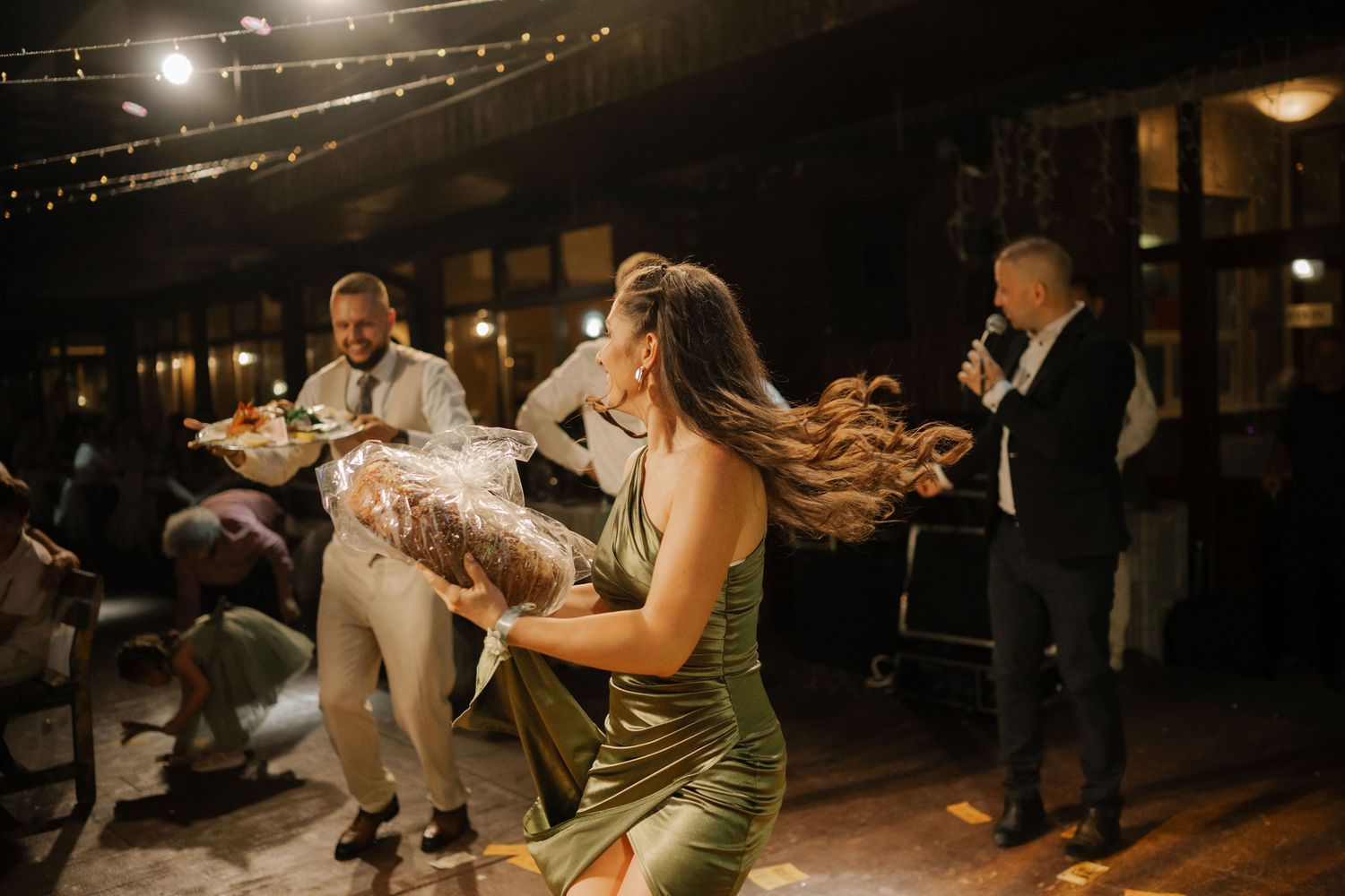 Wedding guests dance together on a rustic wooden dance floor under twinkling string lights at an evening reception.