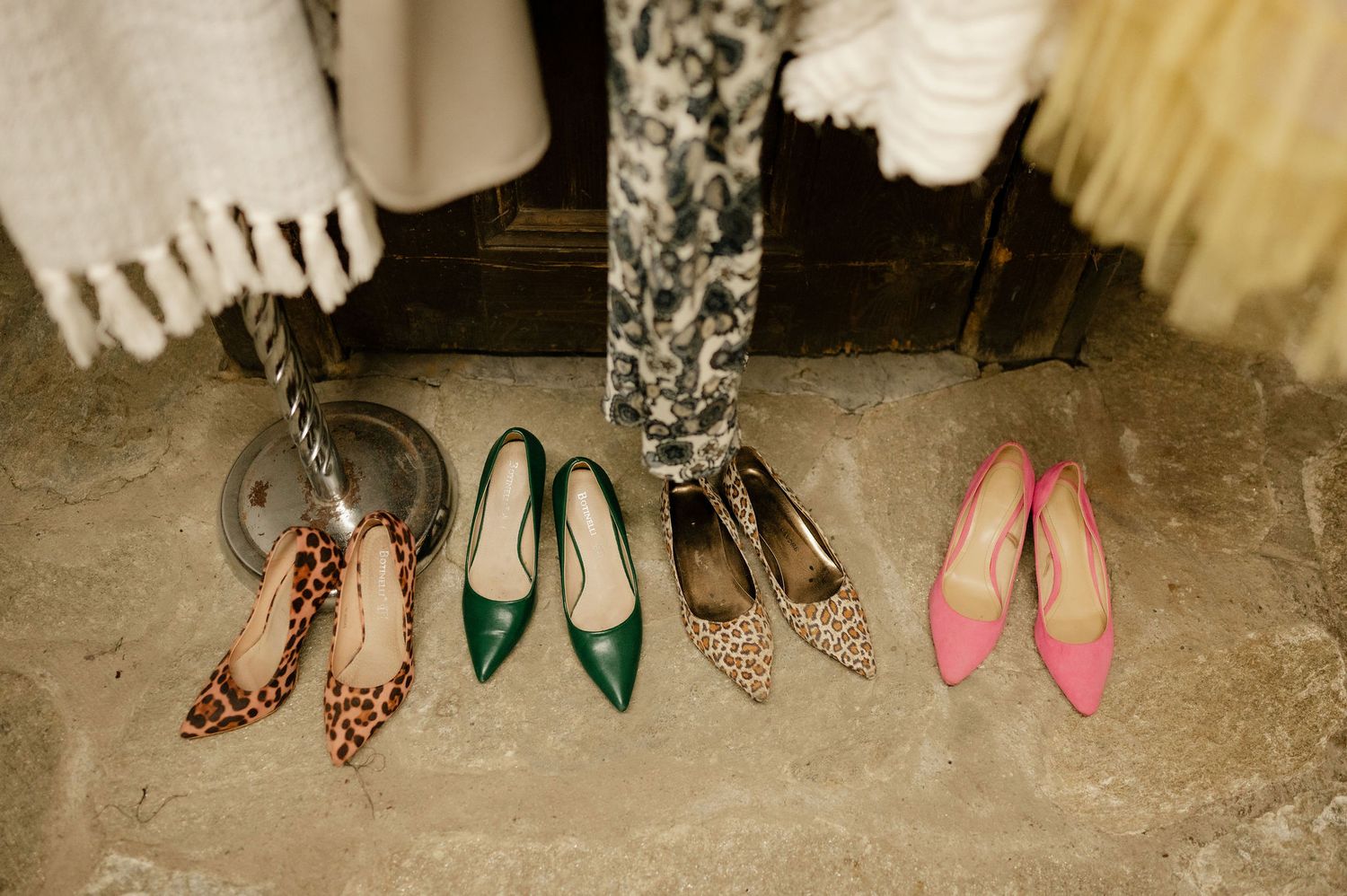 A collection of women's shoes arranged in a line on a rustic floor, featuring various styles and colors.