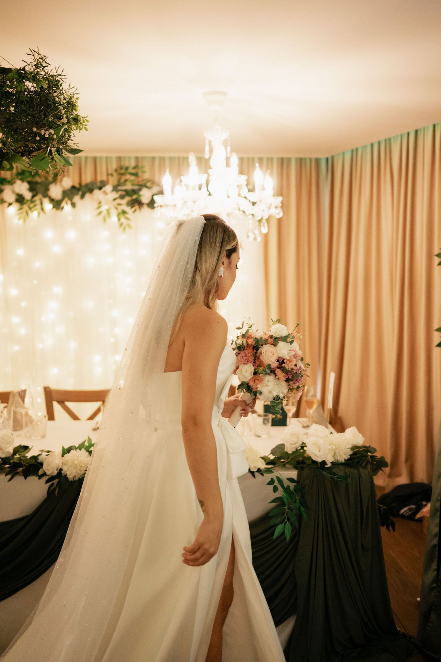 Elegant wedding venue with flowing white veil, crystal chandelier, and soft beige curtains creating a romantic atmosphere.