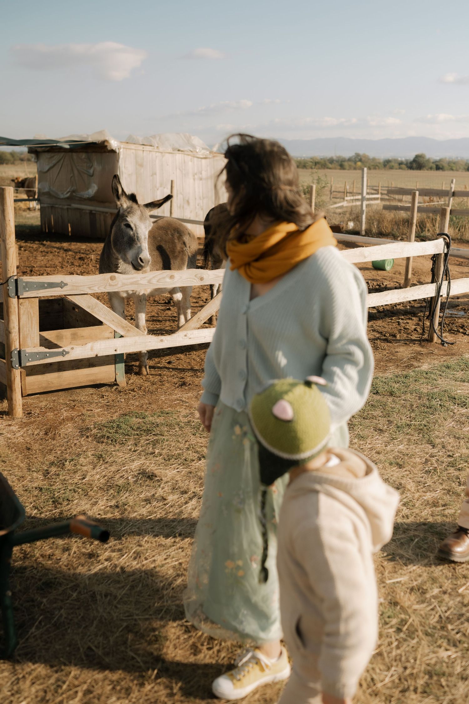 A person in a light-colored sweater hugs a large plush teddy bear in a rural outdoor setting at sunset.