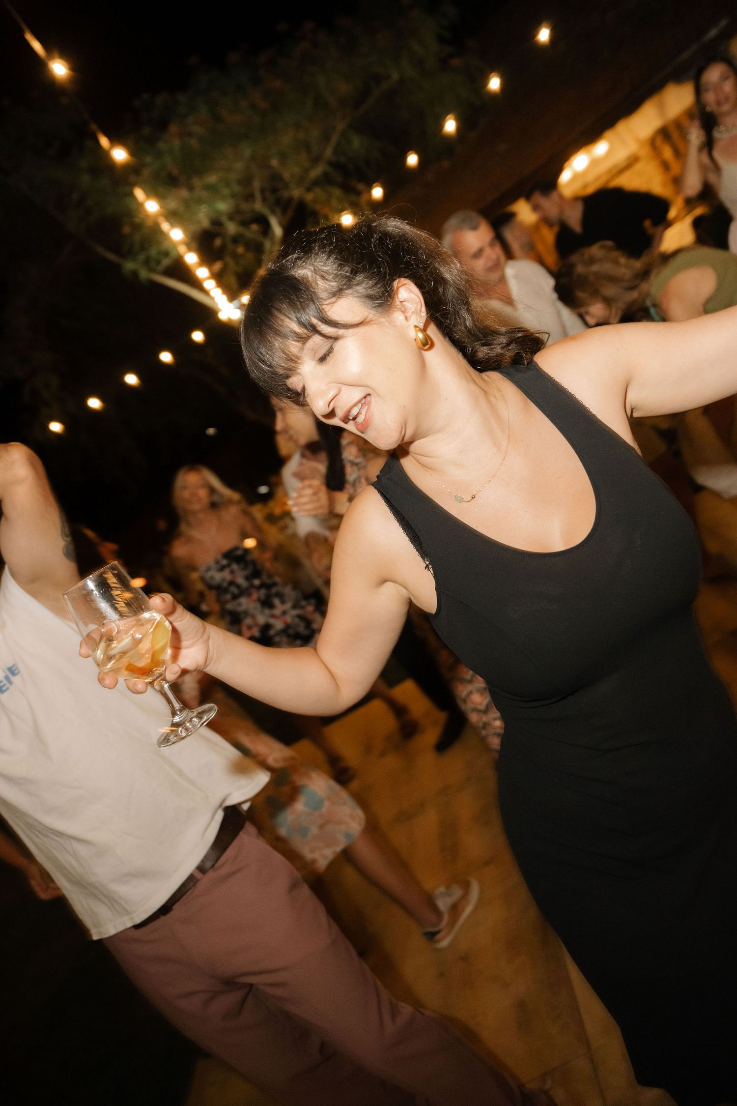 People dancing together at an outdoor evening party with string lights overhead creating a festive atmosphere.