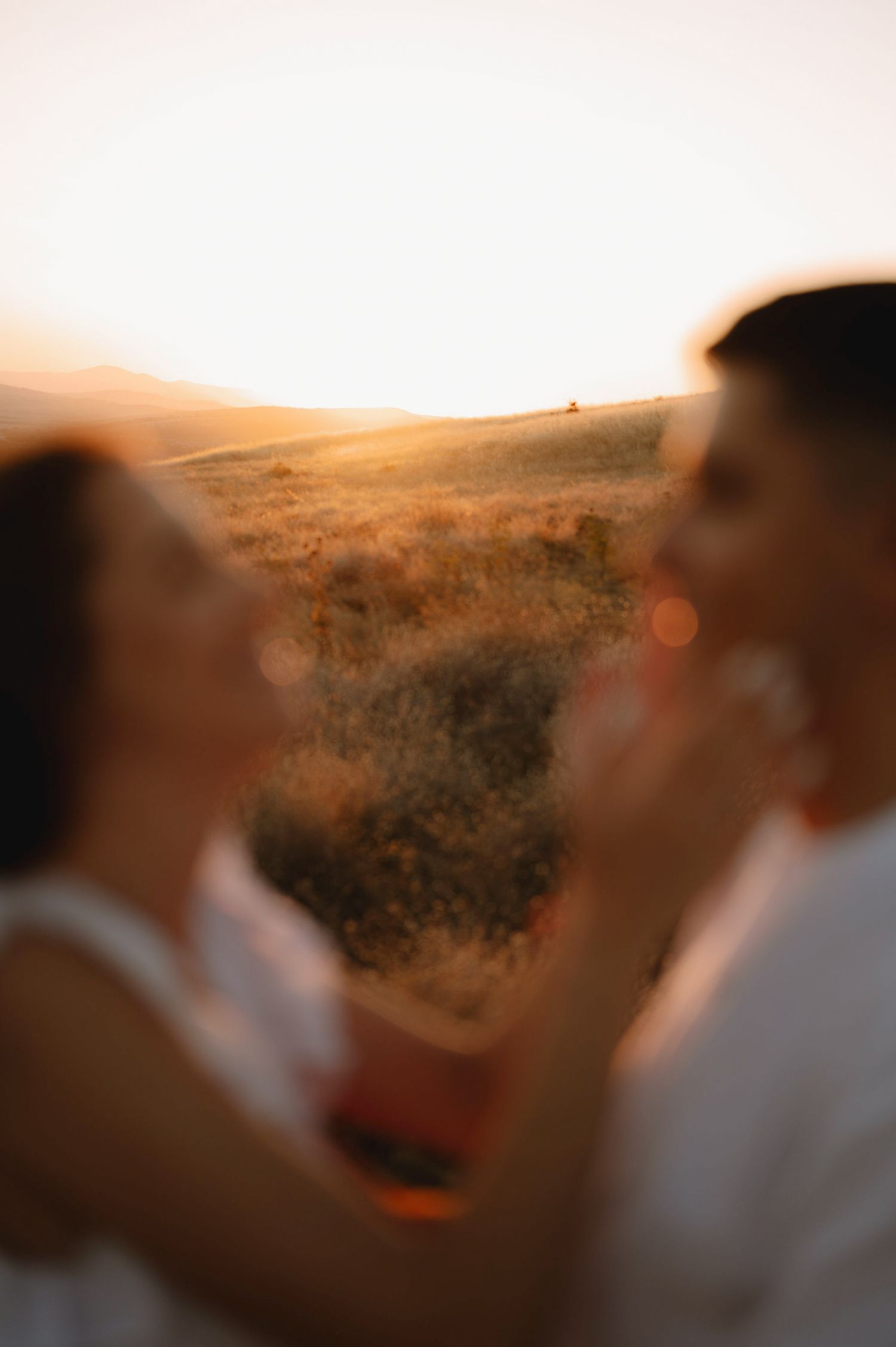 Two silhouettes of people enjoying a scenic mountain sunset with warm golden light in the background.