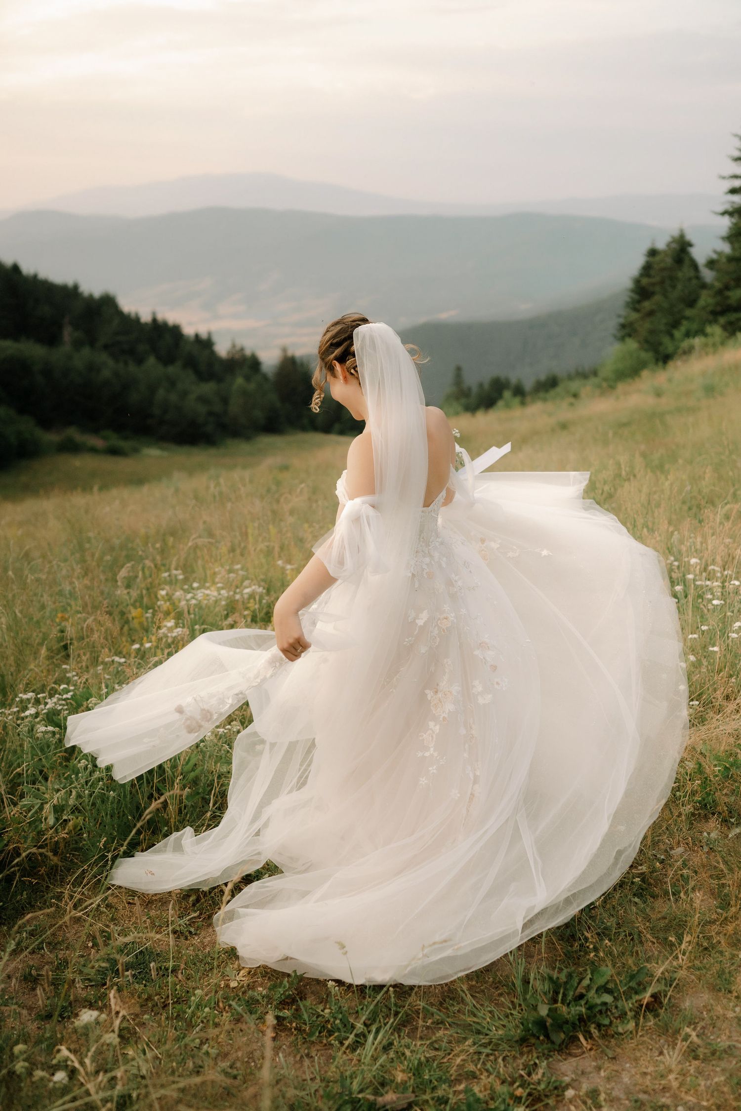 A flowing white wedding dress twirls gracefully across a mountain meadow in a series of ethereal movement shots.