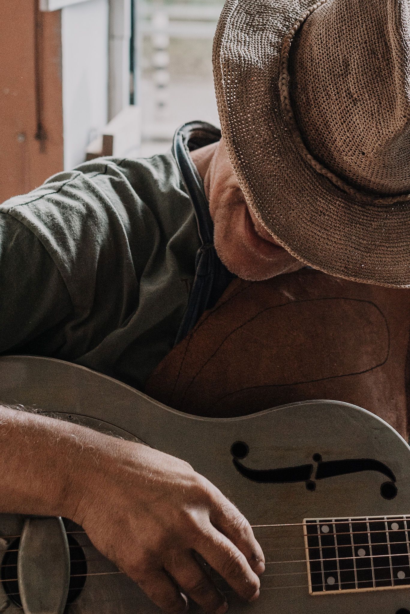 Close-up view of hands playing an acoustic guitar with a brown hat visible in frame.