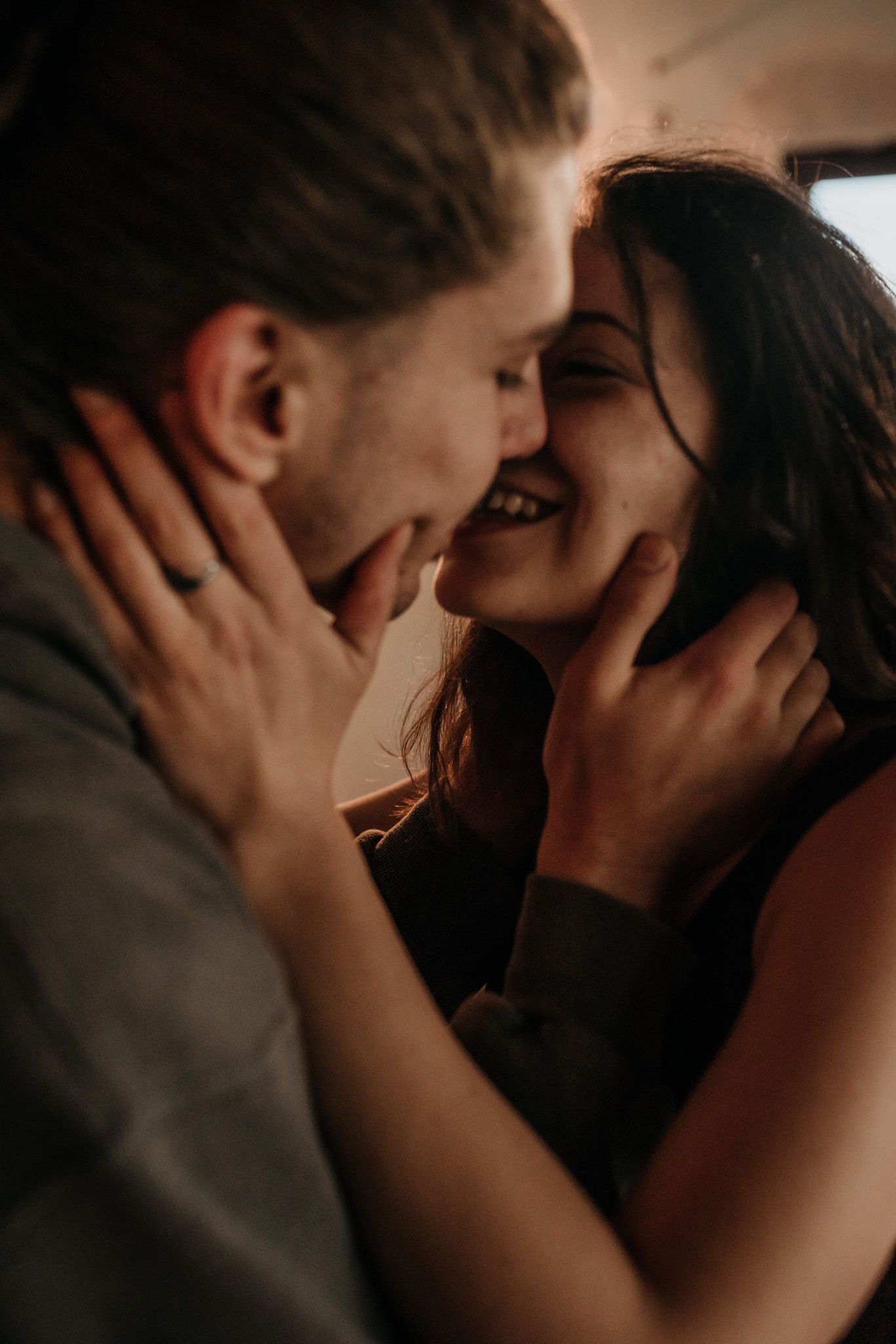 A romantic couple sharing an intimate kiss in moody lighting with hands tenderly touching faces.