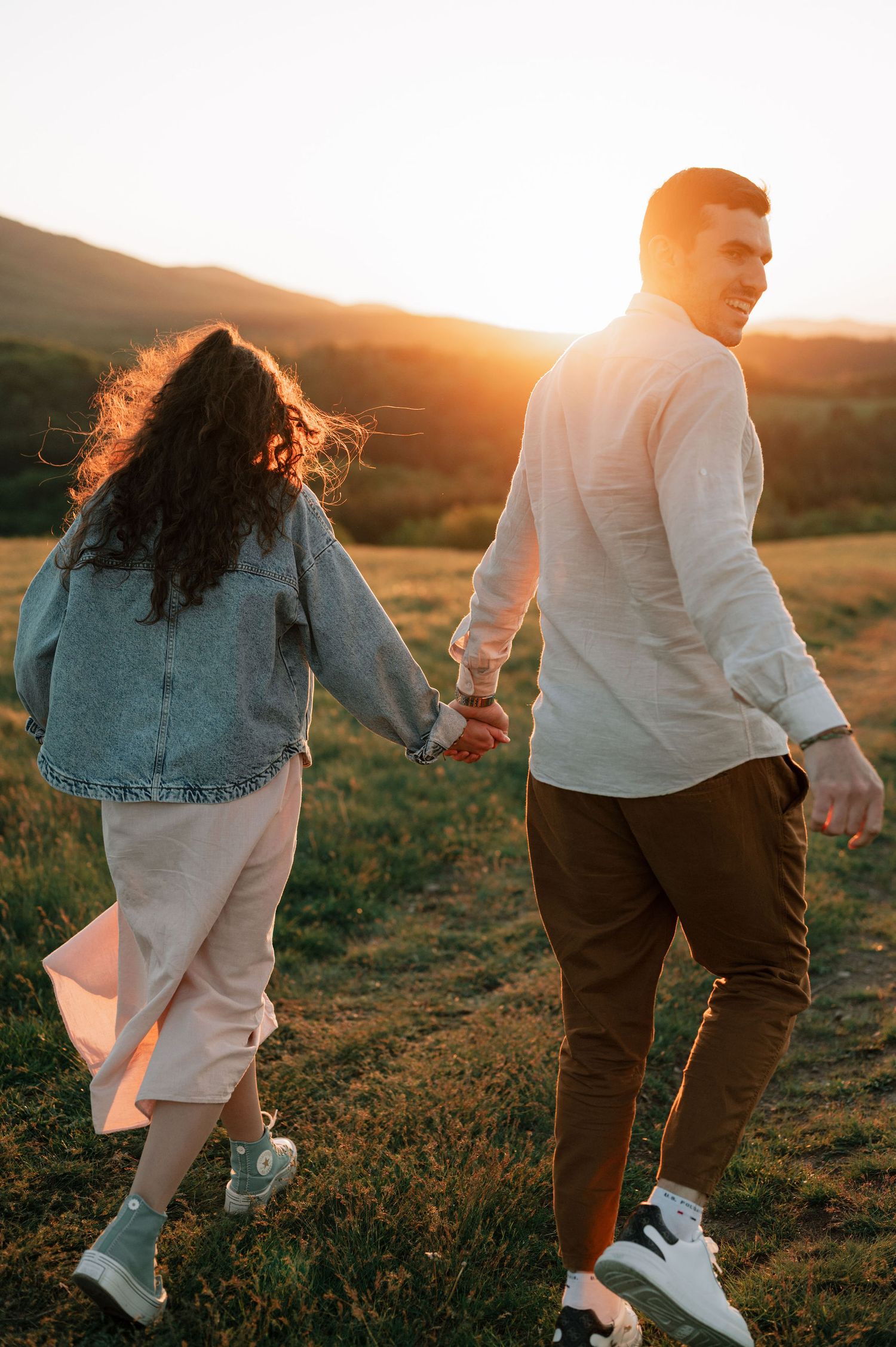 A couple holds hands while walking through a golden field at sunset, captured in a series of candid romantic shots.
