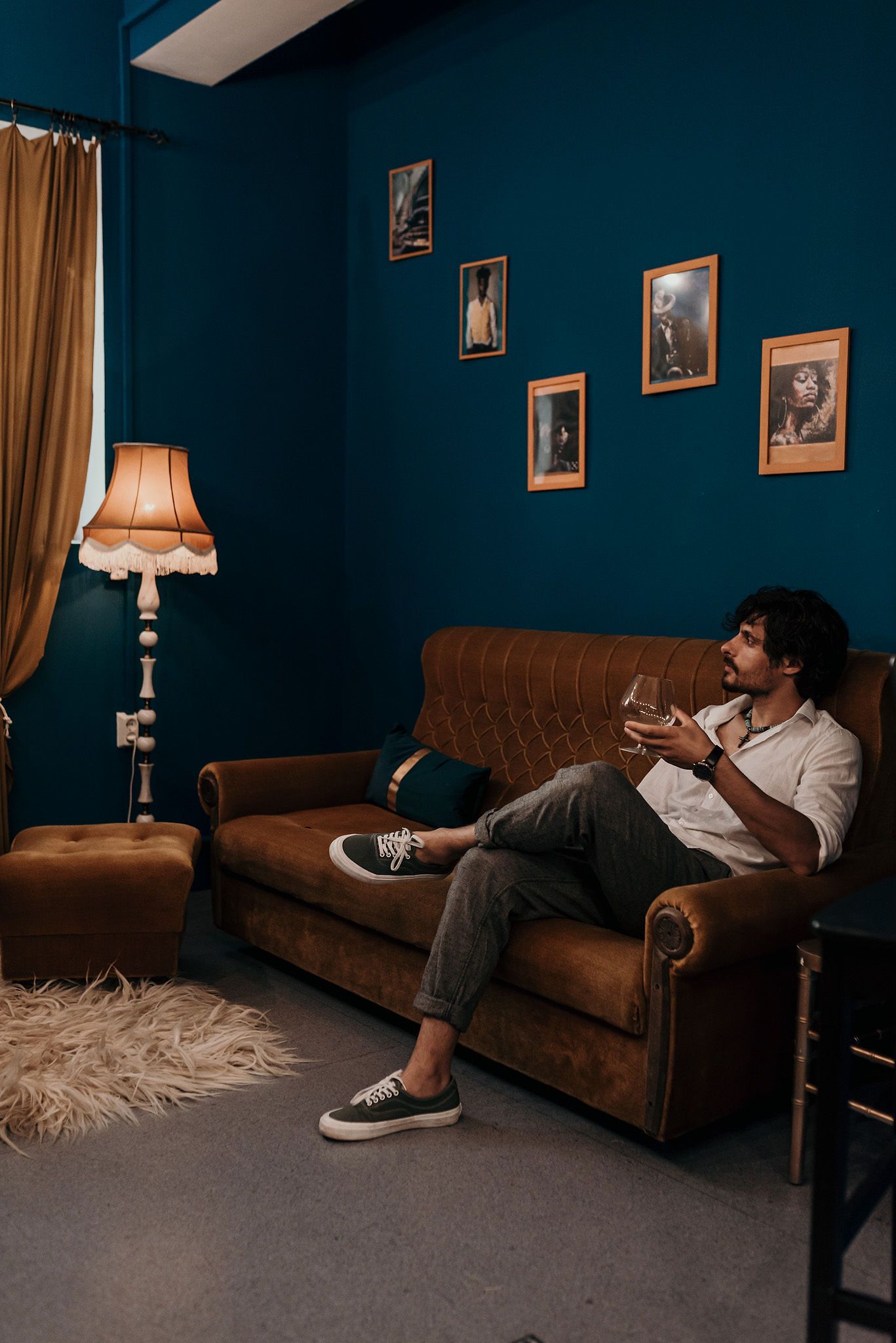 Moody interior scene with brown leather couch against deep teal walls and vintage table lamps creating atmospheric lighting.