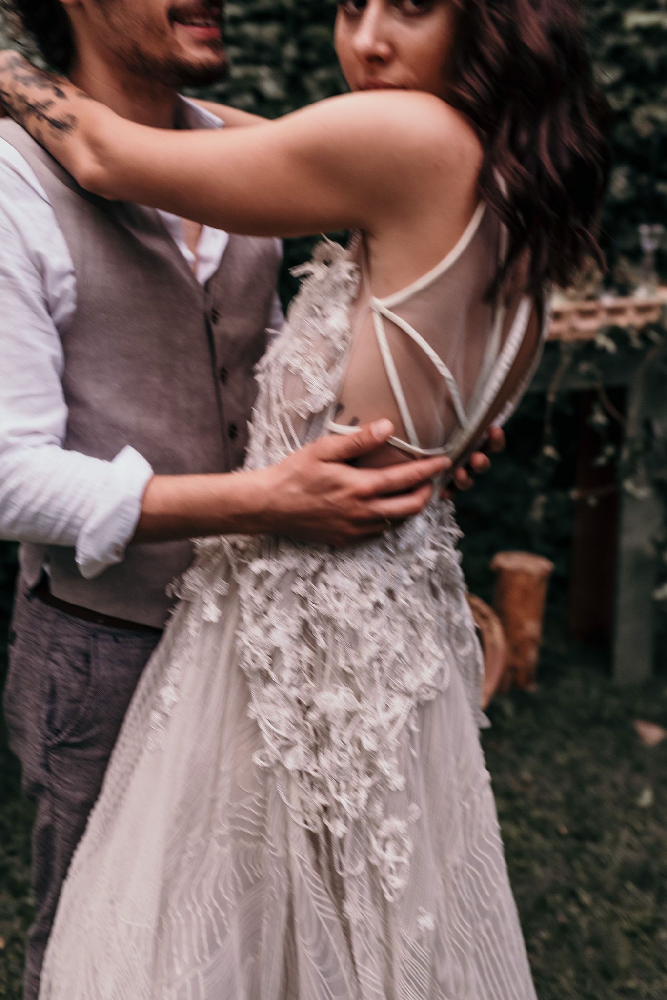 Close up of a couple embracing in wedding attire, showing intricate lace details on a flowing white bridal gown.