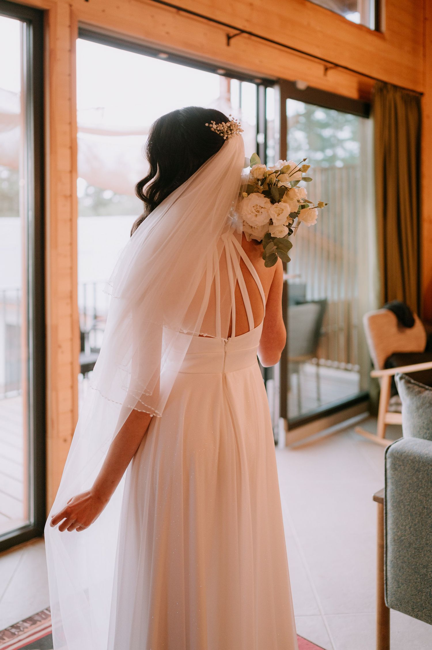Side view of bride in white dress and veil against rustic wooden walls and windows.