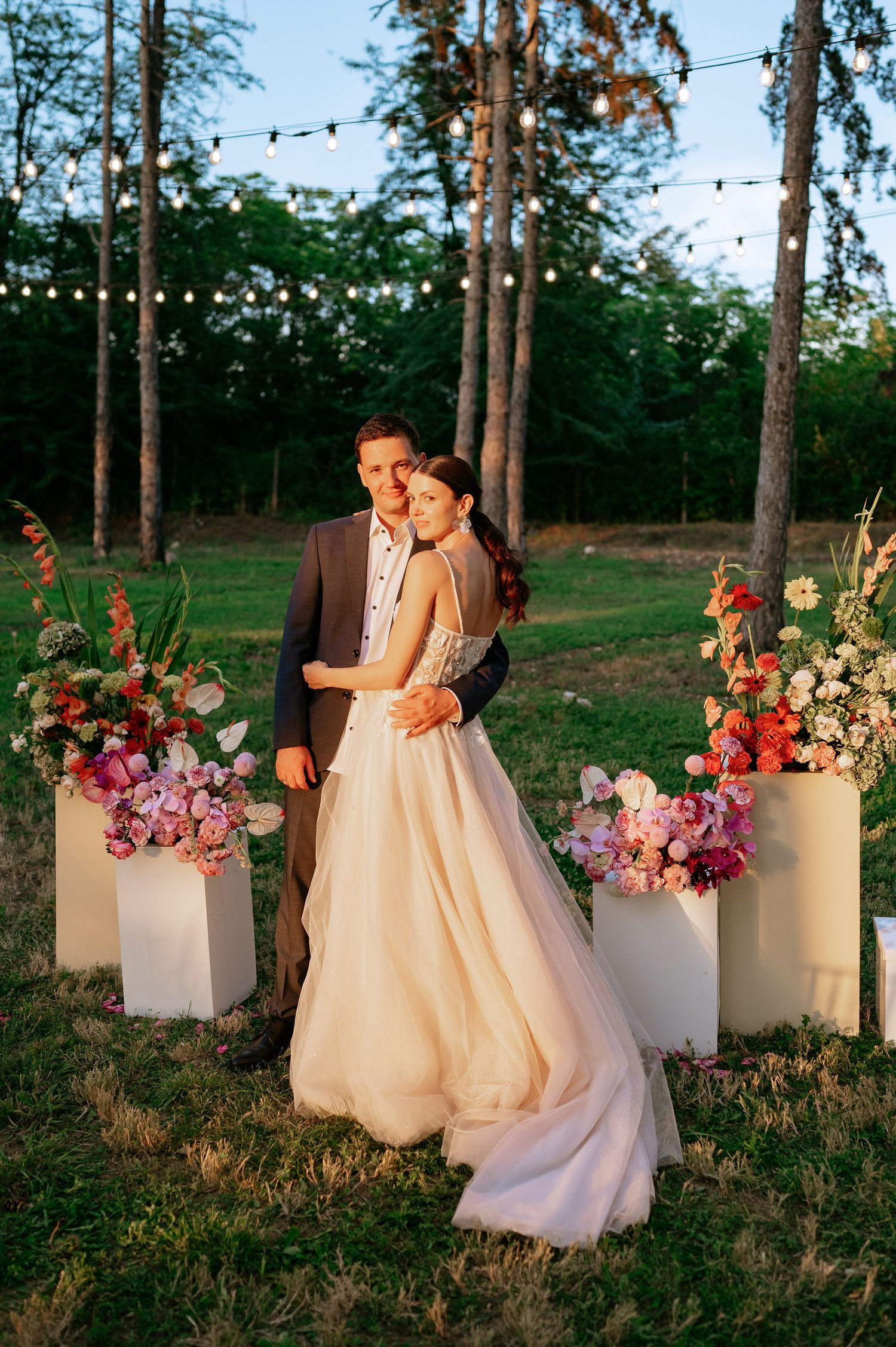 Newlyweds share a romantic moment among floral arrangements at their outdoor forest wedding.