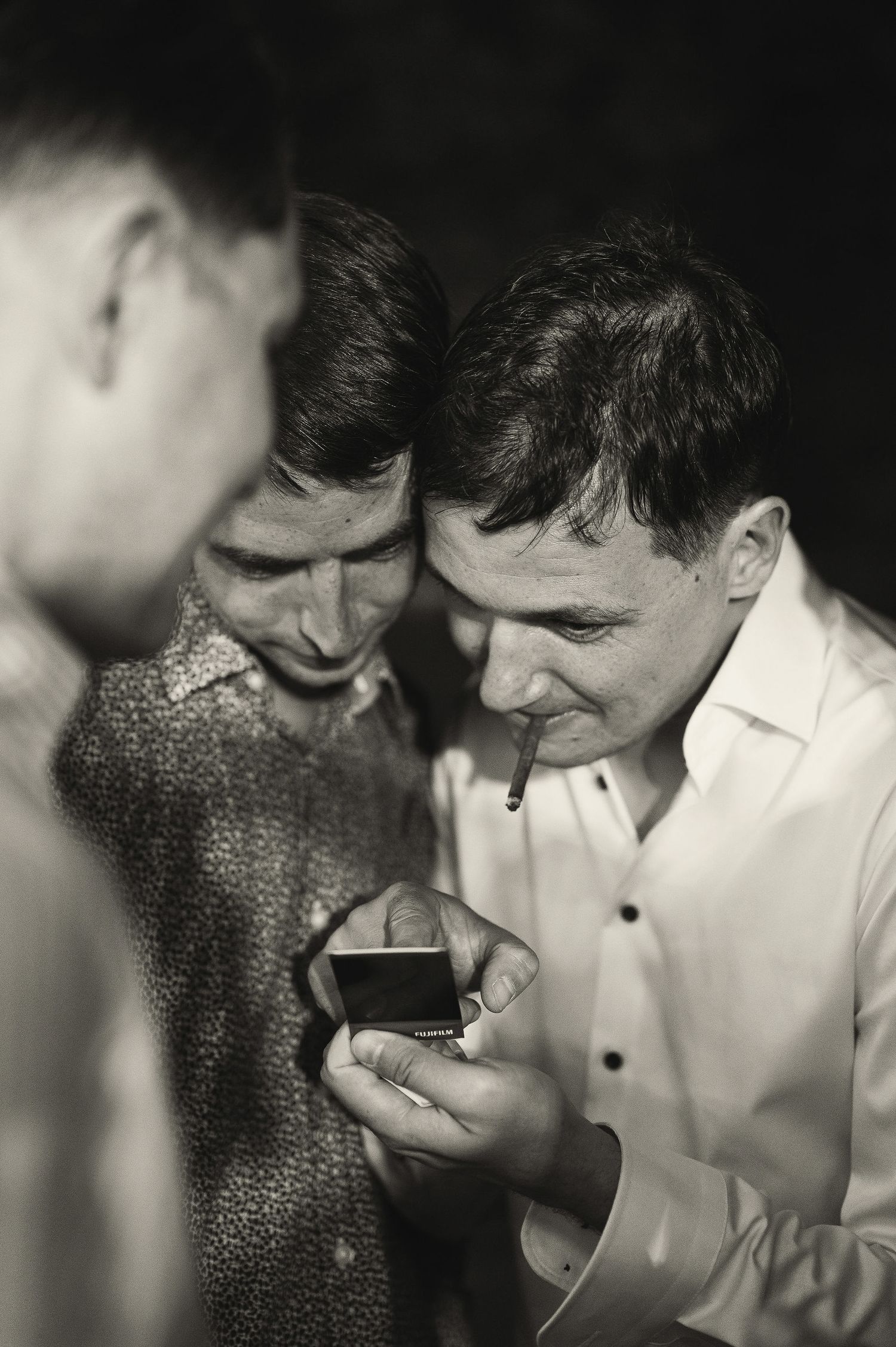 Black and white photo of guests huddled together looking at something small.