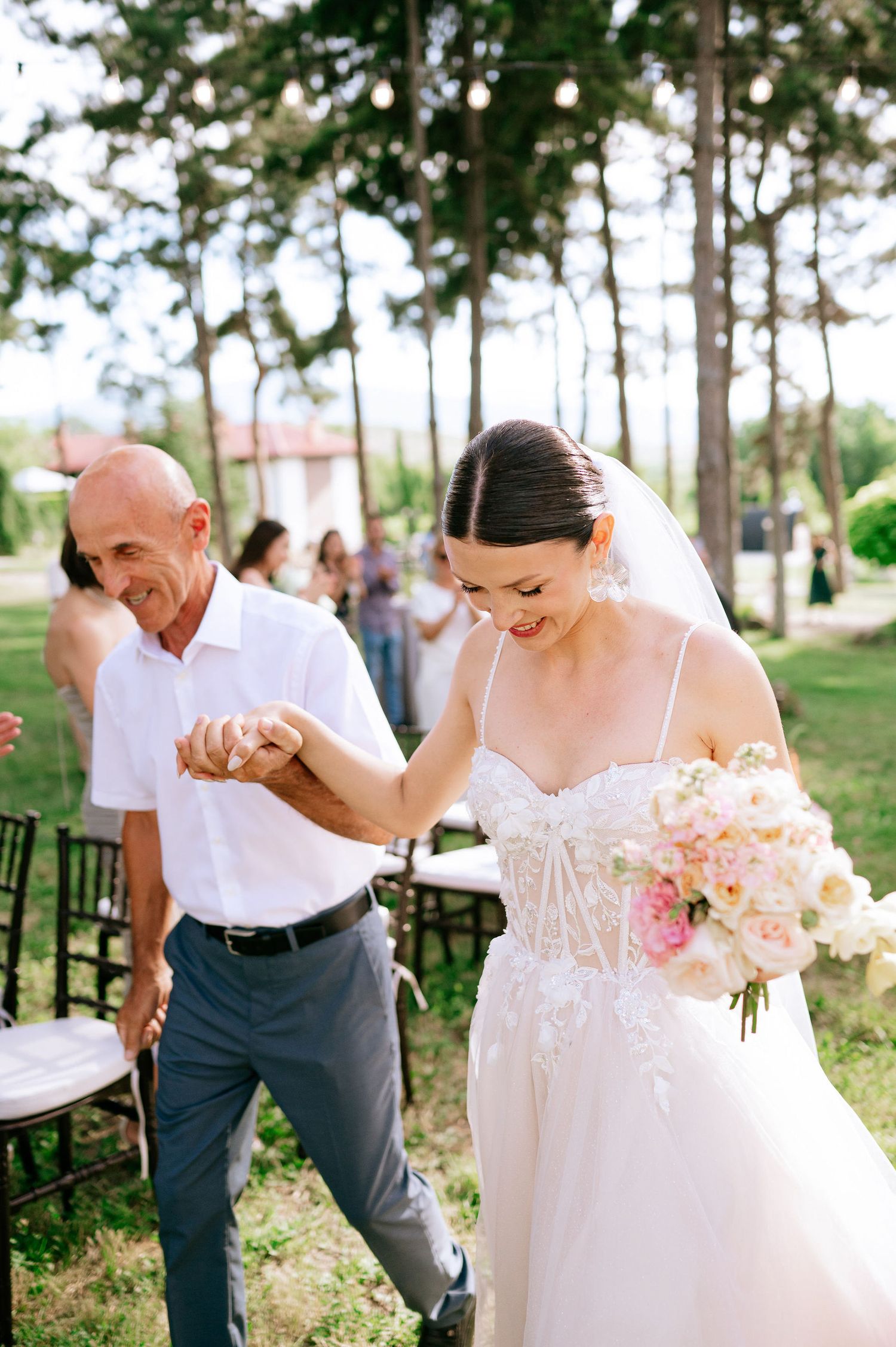 Elegant outdoor wedding scene with floral bouquet and white dress among tall pine trees.