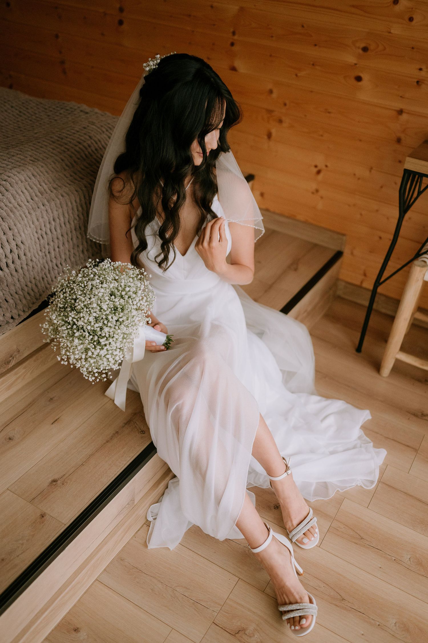 Elegant bridal portrait featuring white dress and sandals against rustic wood flooring.