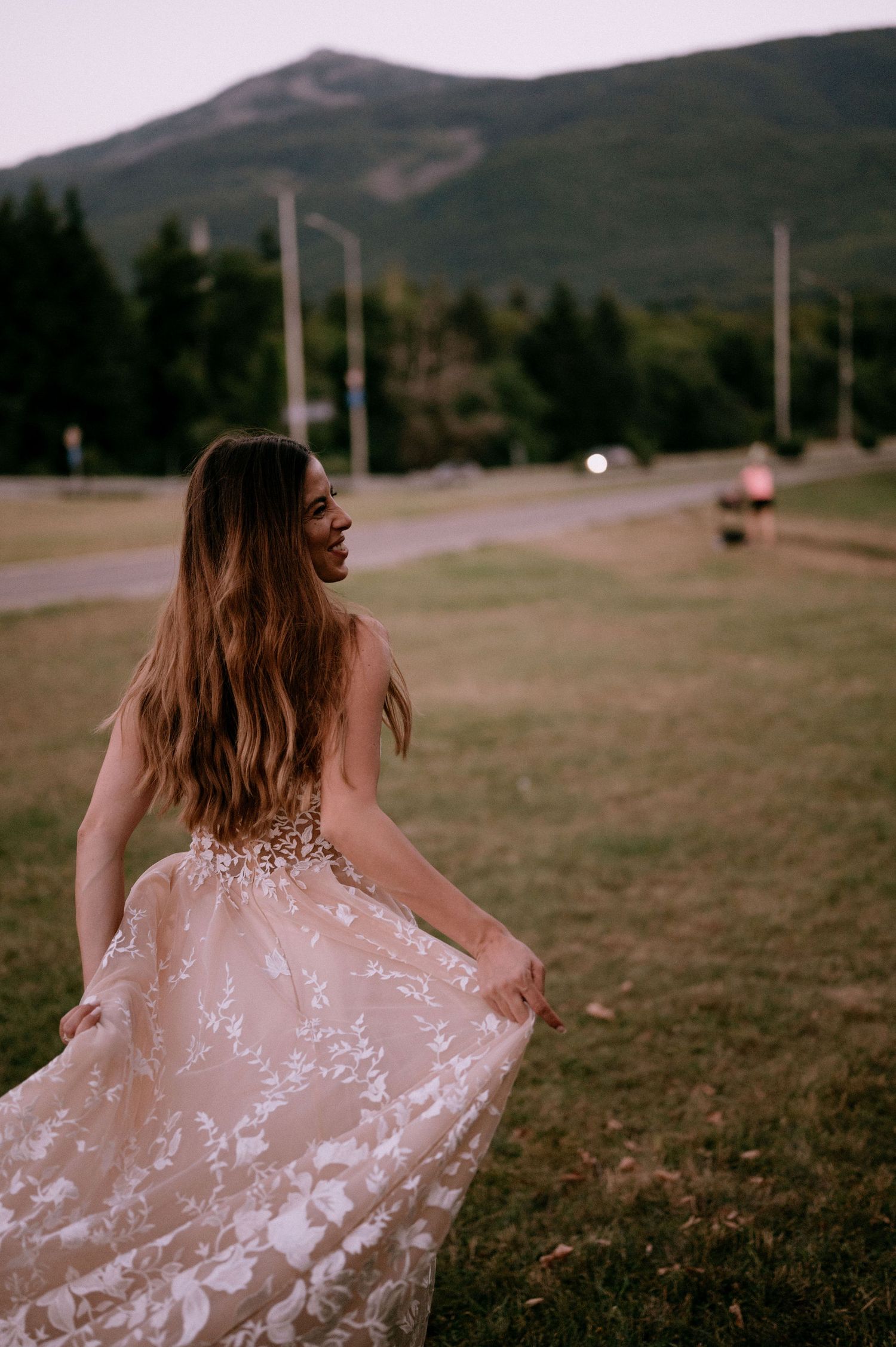 Woman in flowing blush lace dress twirling against mountain landscape.