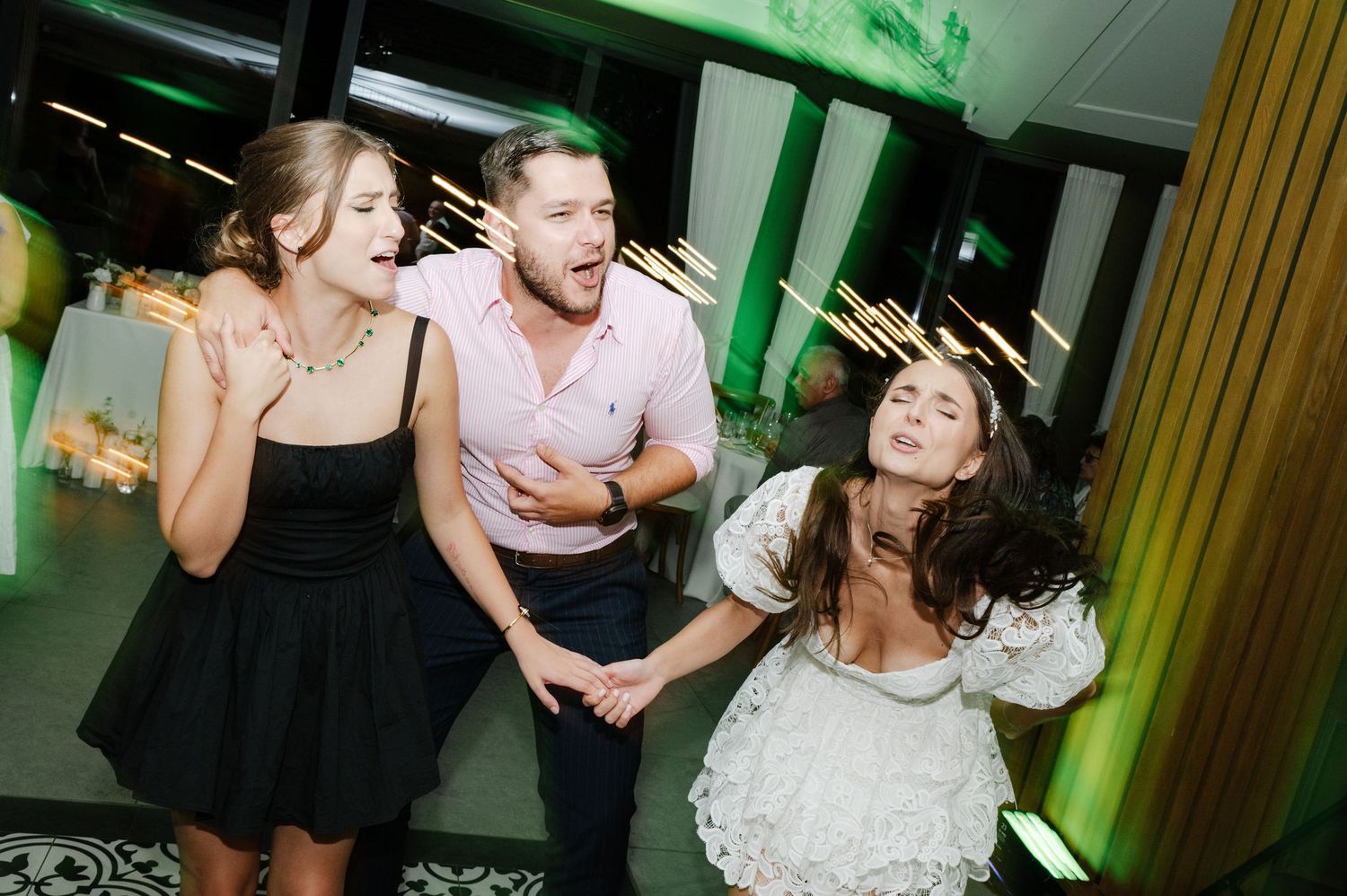 Wedding guests dancing and celebrating on a dance floor with green ambient lighting.