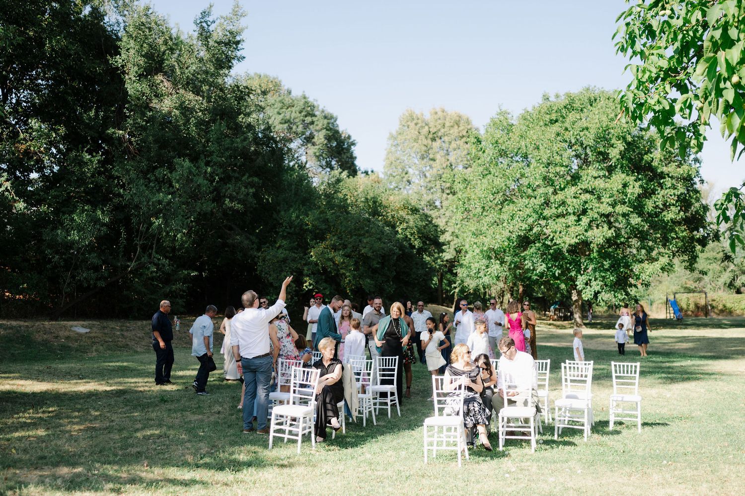 White chairs arranged in rows for an outdoor ceremony under green trees.
