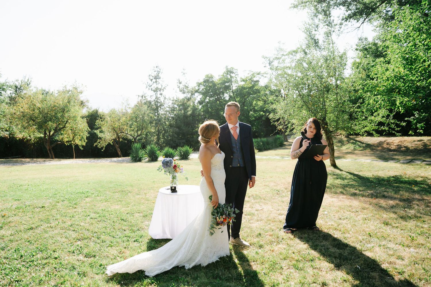 Wedding couple walks through a sunny outdoor garden setting with lush greenery.
