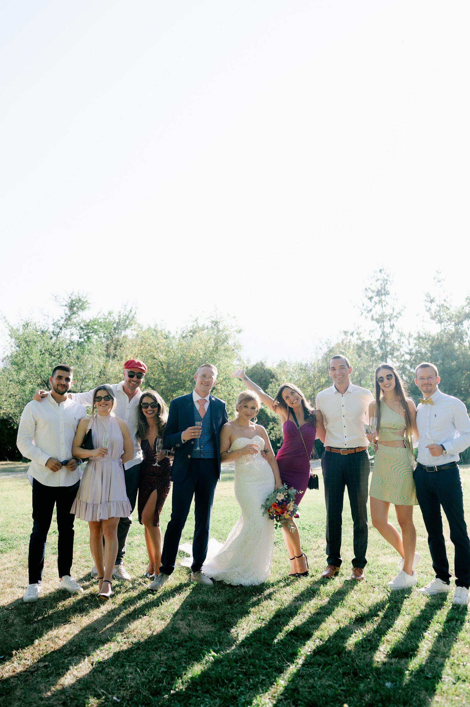 Group photo of wedding attendees lined up outdoors with dramatic backlighting creating silhouettes.