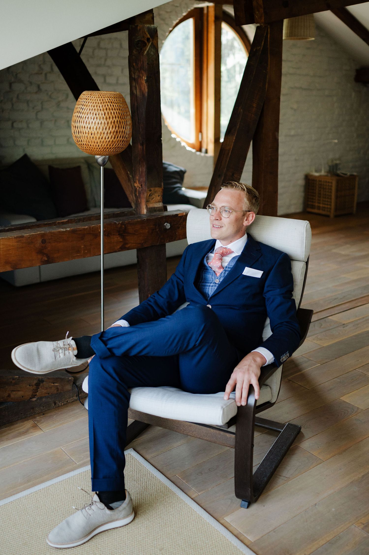 Someone lounges in a modern chair wearing formal attire in a rustic attic setting.