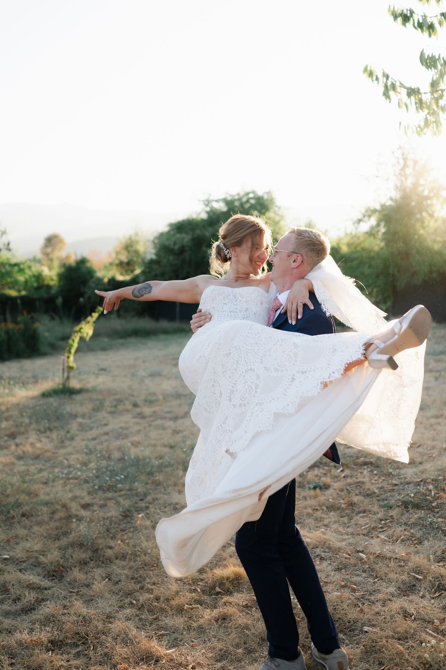 Groom dips bride in flowing white dress during sunset wedding photos in an outdoor setting.