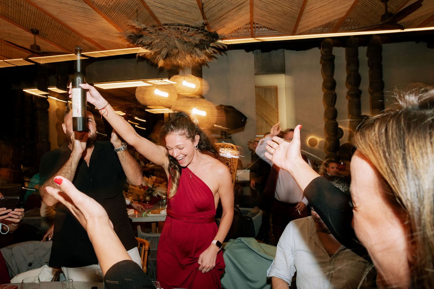 Wedding guests dancing enthusiastically on a dimly lit dance floor at an indoor reception.