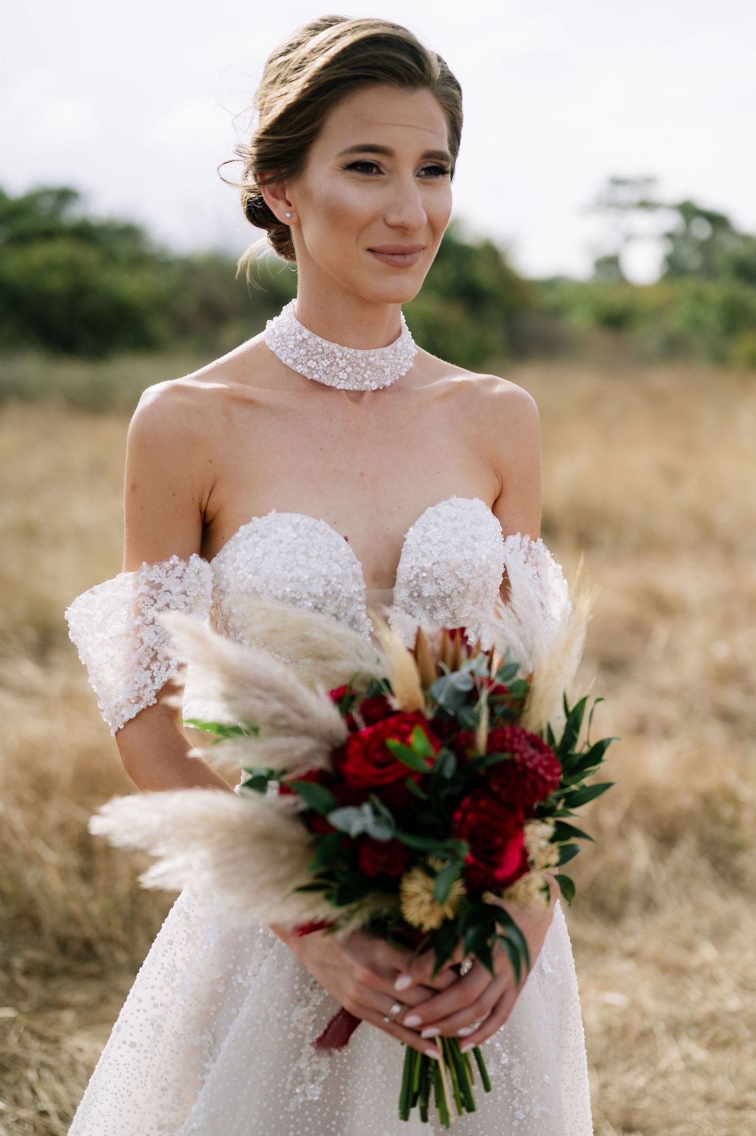 Close-up portrait showcasing intricate beading on a white off-shoulder wedding gown with burgundy flowers.