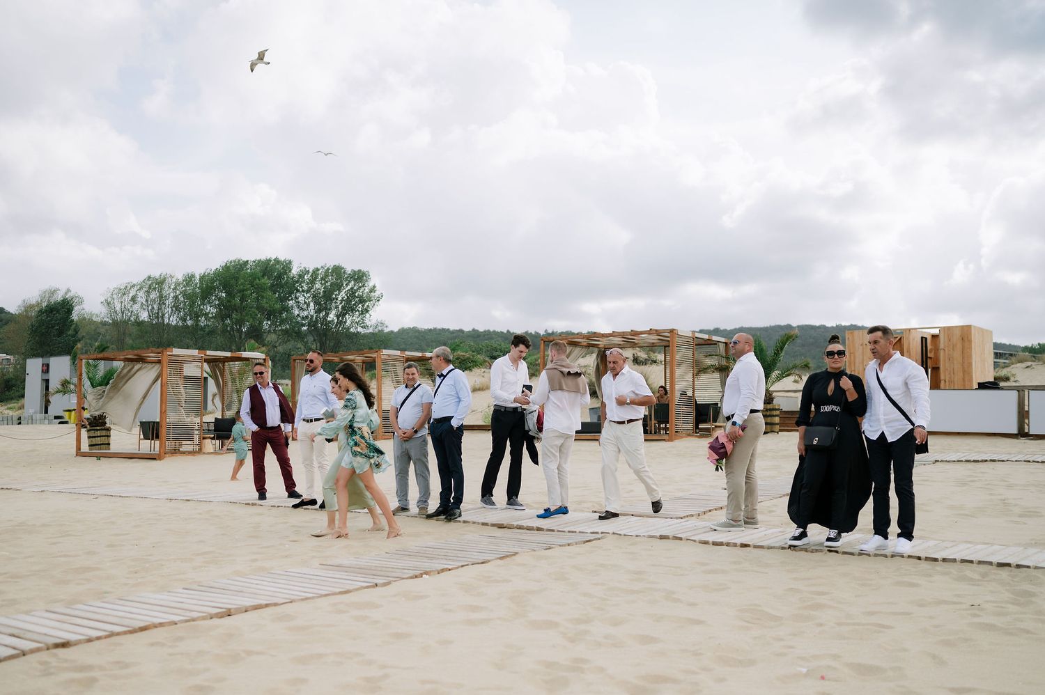 Event guests gather near decorative wooden structures on a beachfront patio.