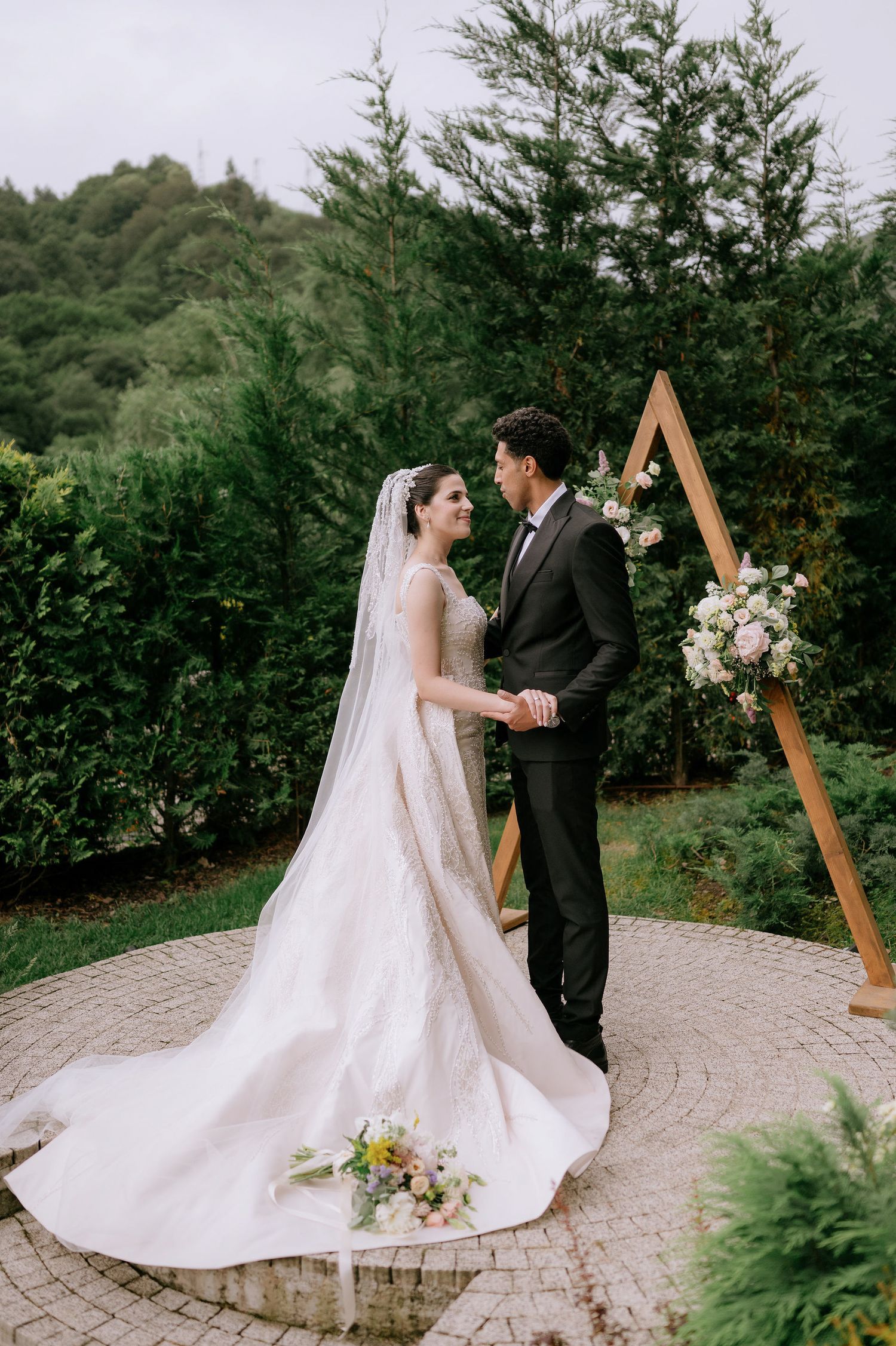 Wedding couple holding hands on a circular stone patio with wooden triangular arch and floral decor.