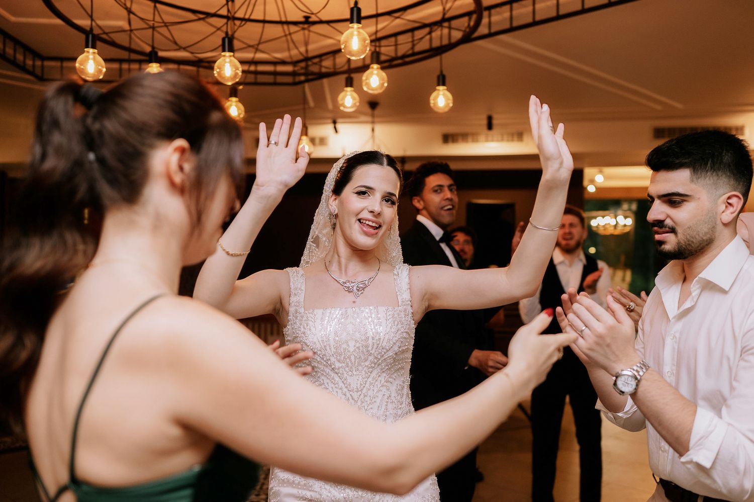 Wedding reception guests dancing and celebrating together in an elegantly lit indoor venue.