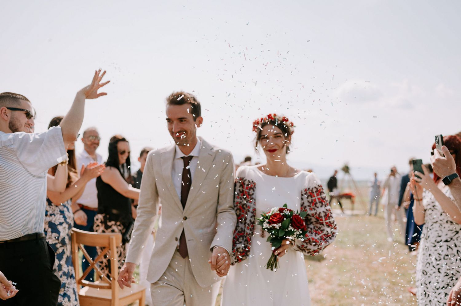 Wedding guests throw confetti as a couple walks down the aisle in a beachside ceremony.