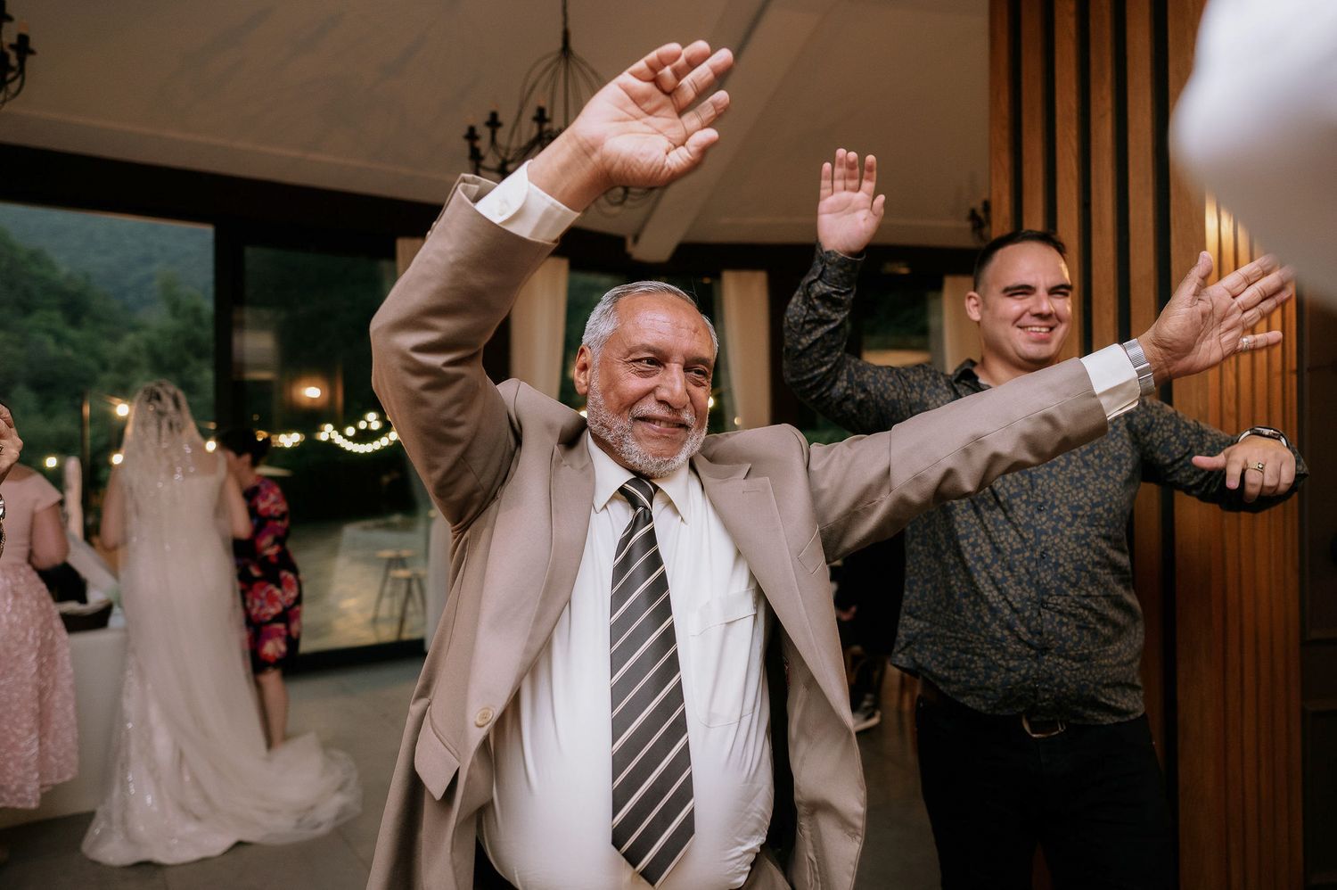 Party guests dancing in formation with their arms raised during a celebration.