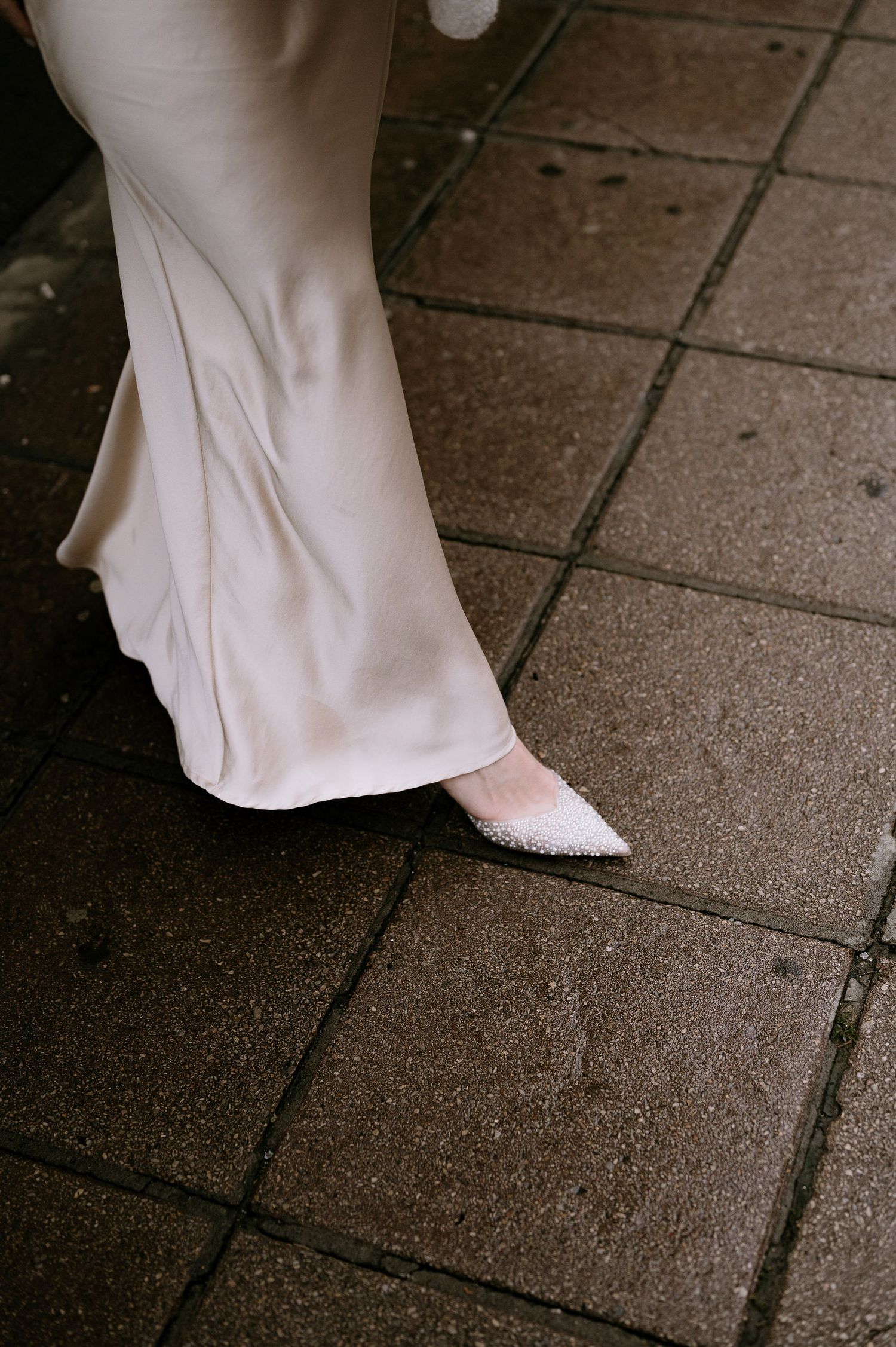 Close-up view of a white dress hem and shoes on stone pavement.