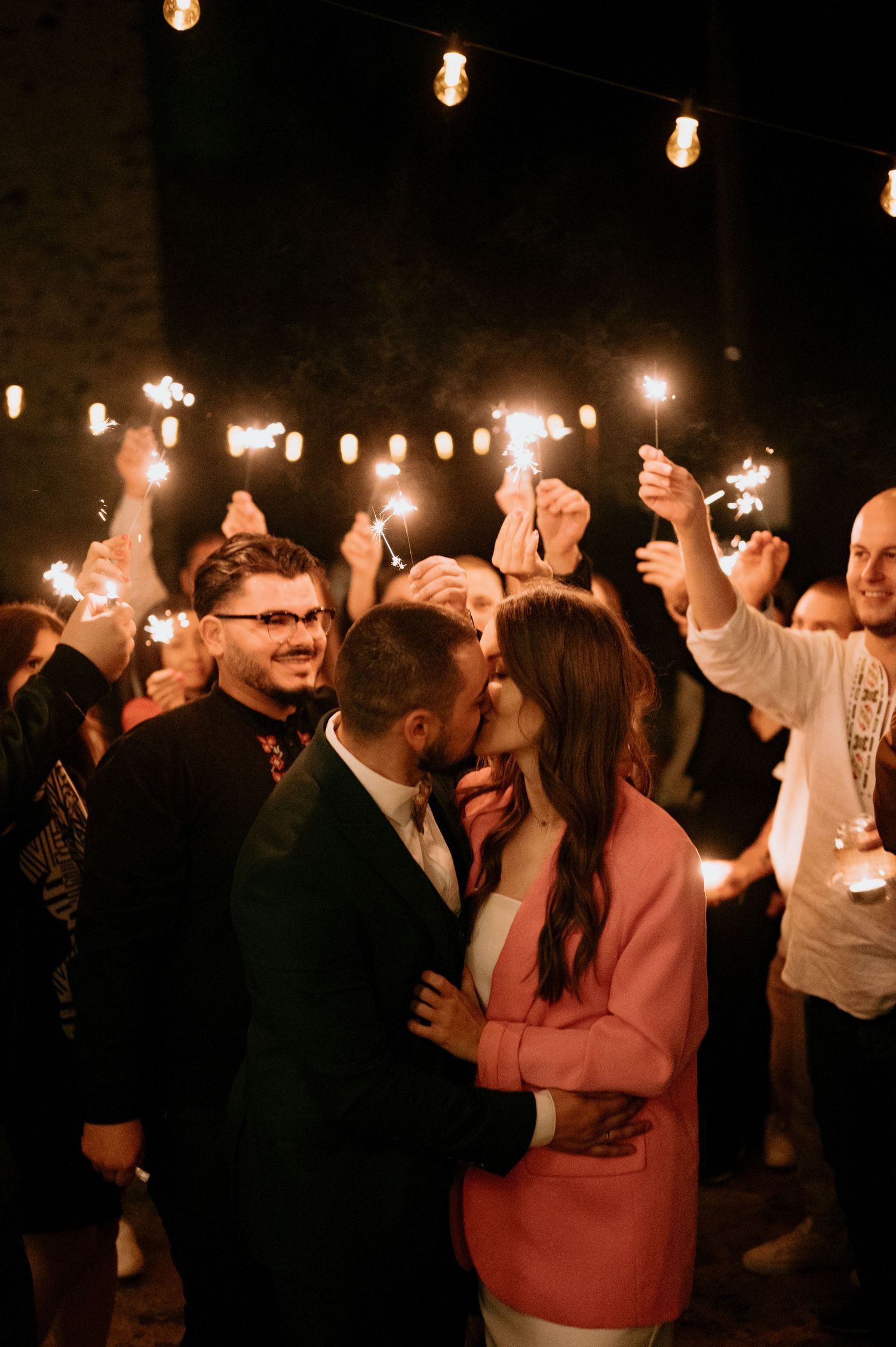Crowd celebrates with sparklers and dancing during a nighttime outdoor party.