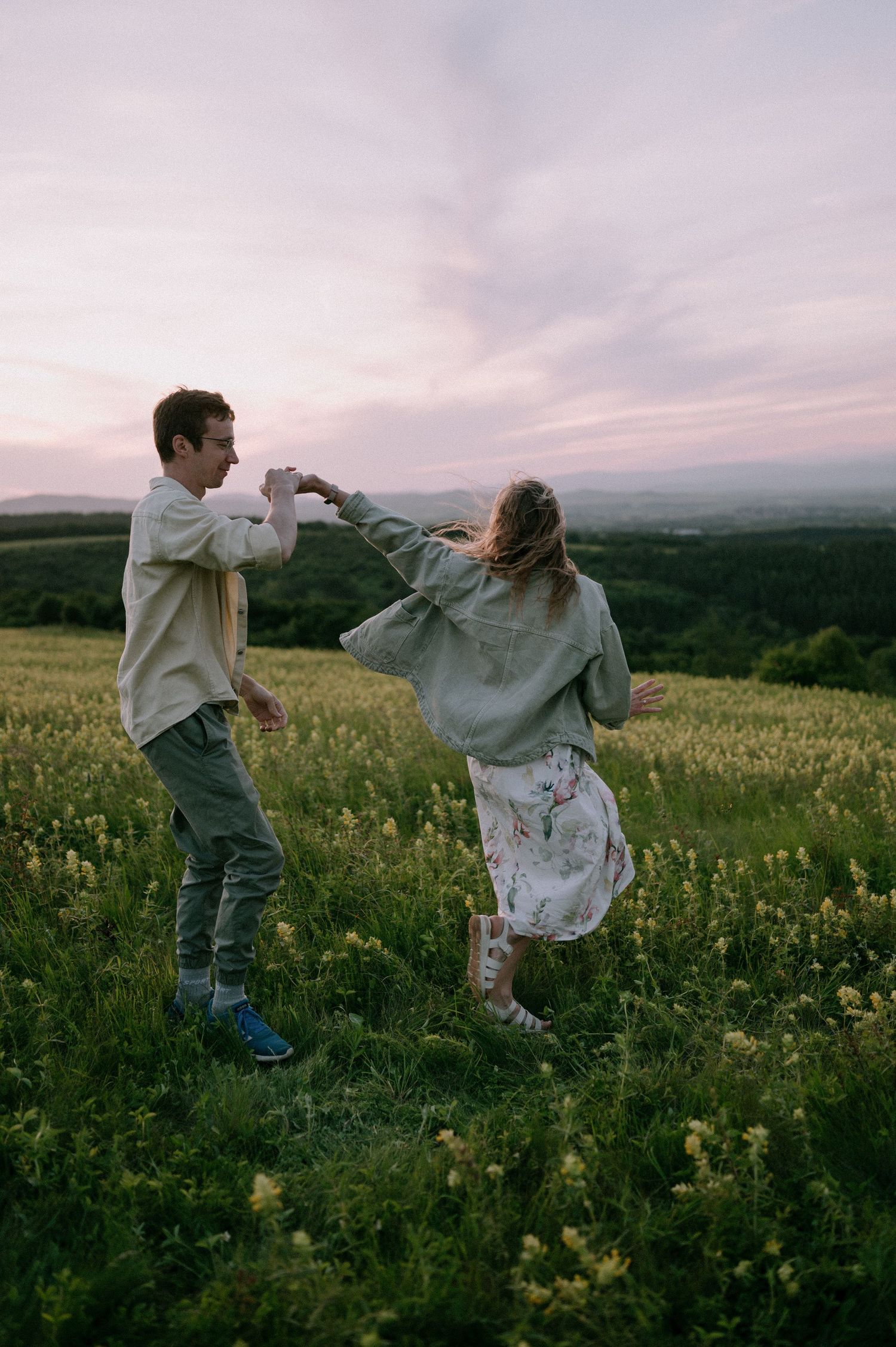 A couple dances freely through a field of wildflowers against a dusky mountain landscape.