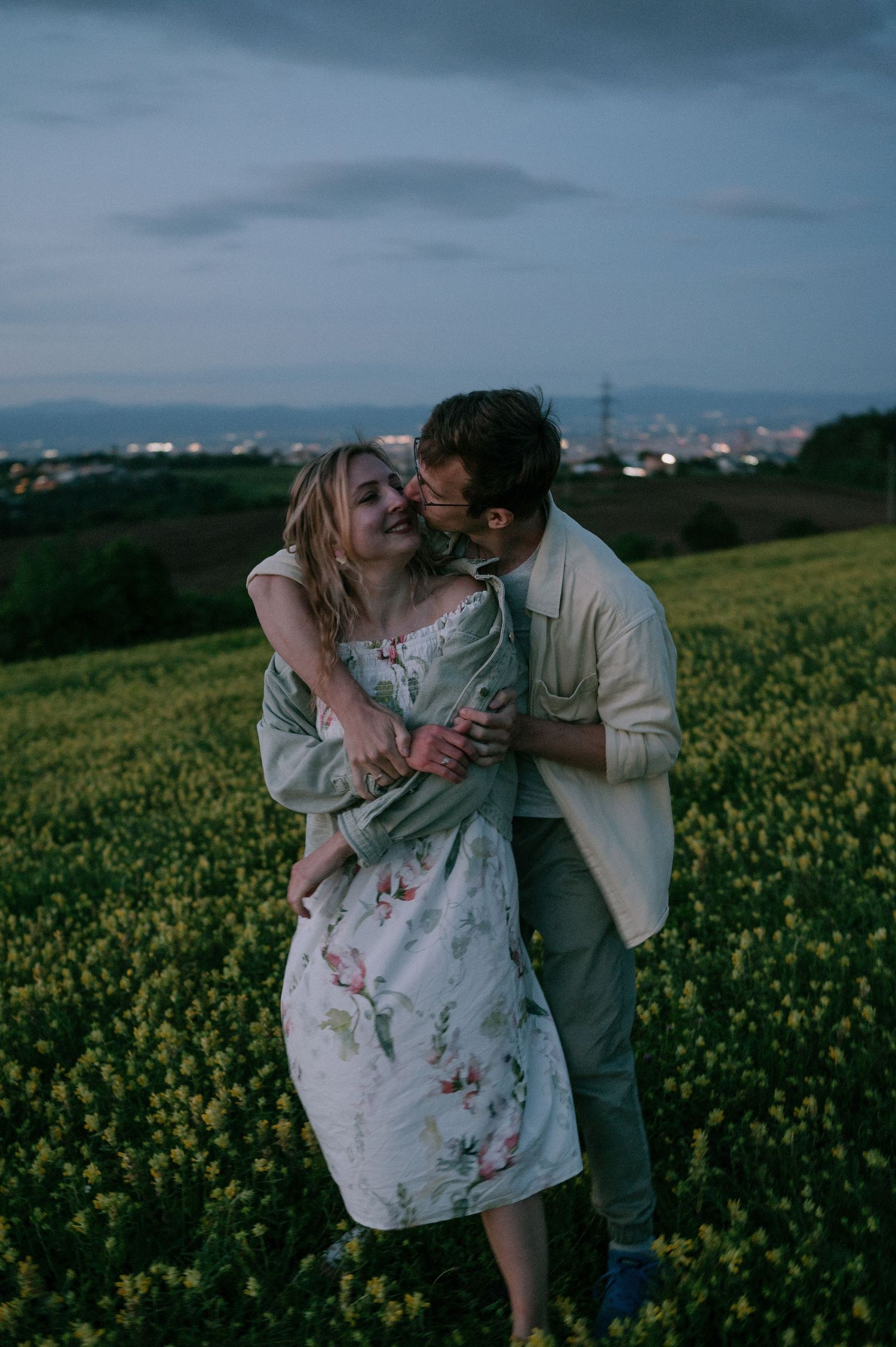 Romantic embrace in blooming yellow flower field under cloudy skies.