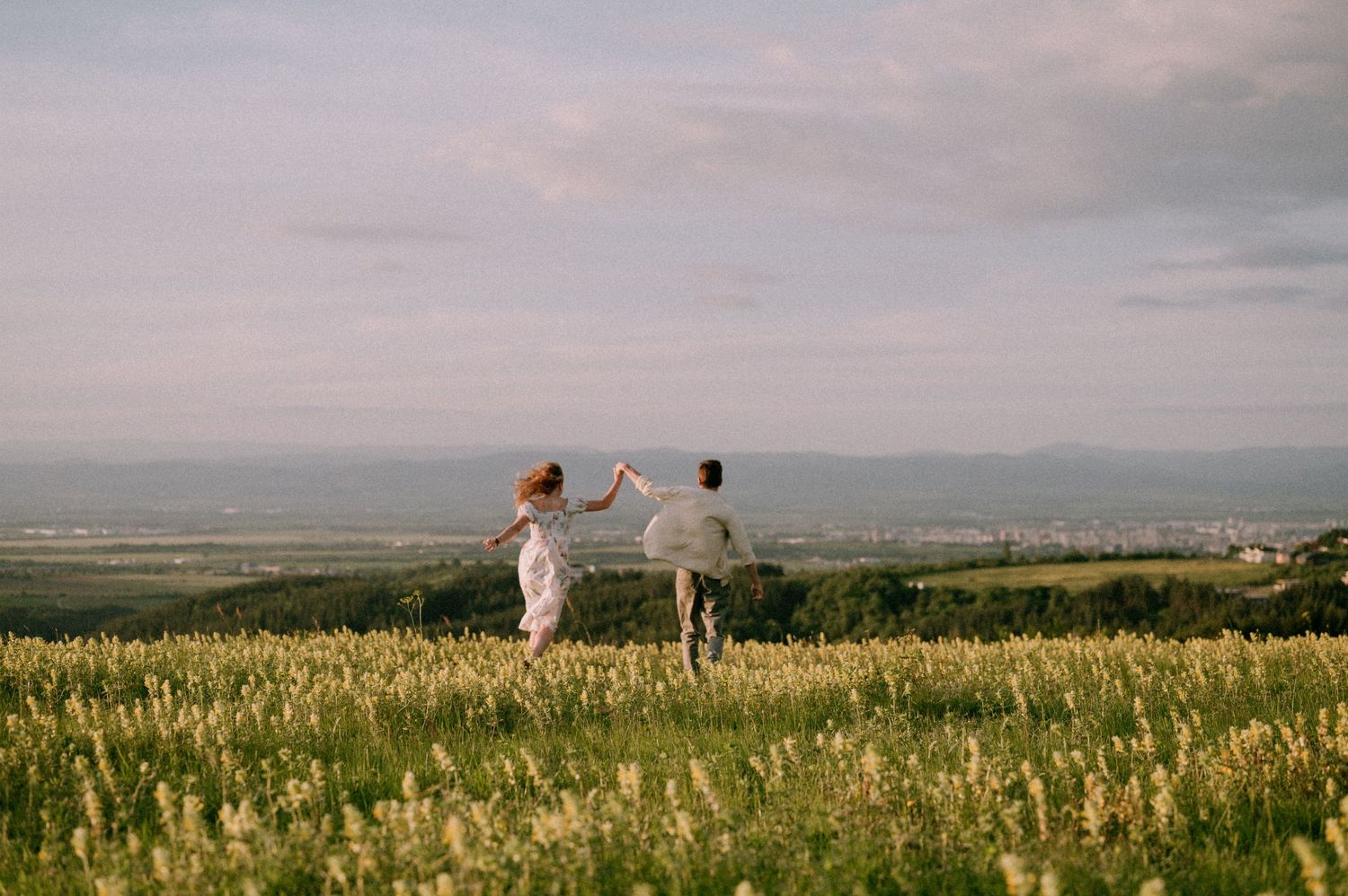 Wide landscape shot of couple in distance dancing in mountain meadow with expansive valley view.