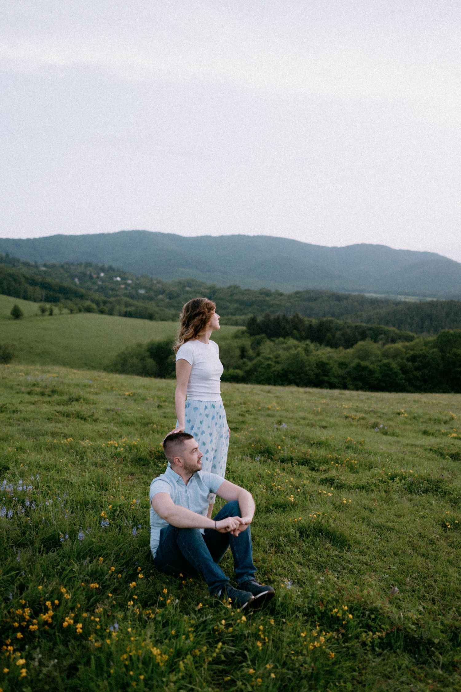 A couple sits together in a scenic mountain meadow filled with wildflowers at sunset.