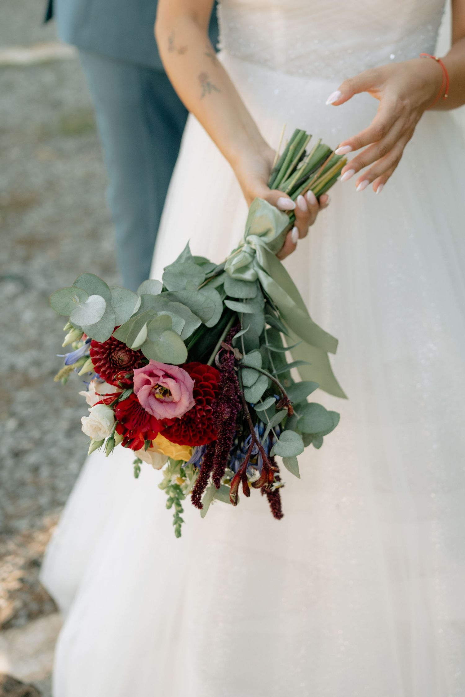 Wedding bouquet with deep burgundy and pink flowers paired with silvery eucalyptus leaves against a white dress.