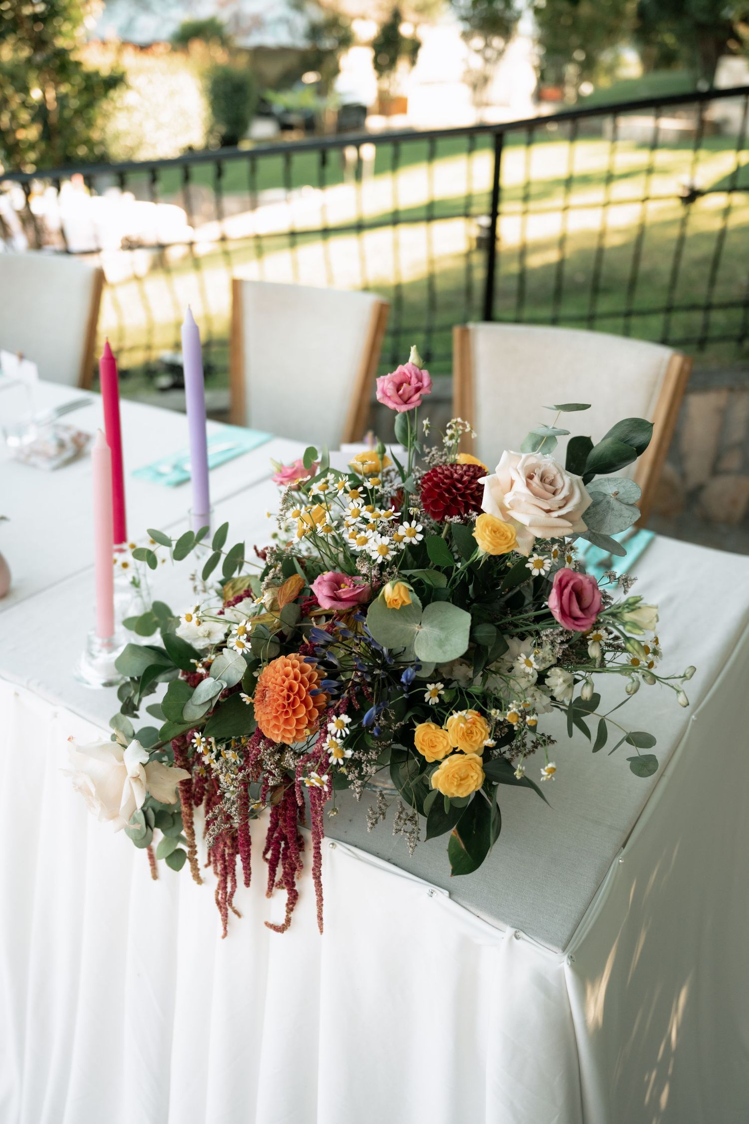 Elegant floral centerpiece with roses, dahlias and eucalyptus on white tablecloth at outdoor wedding reception.