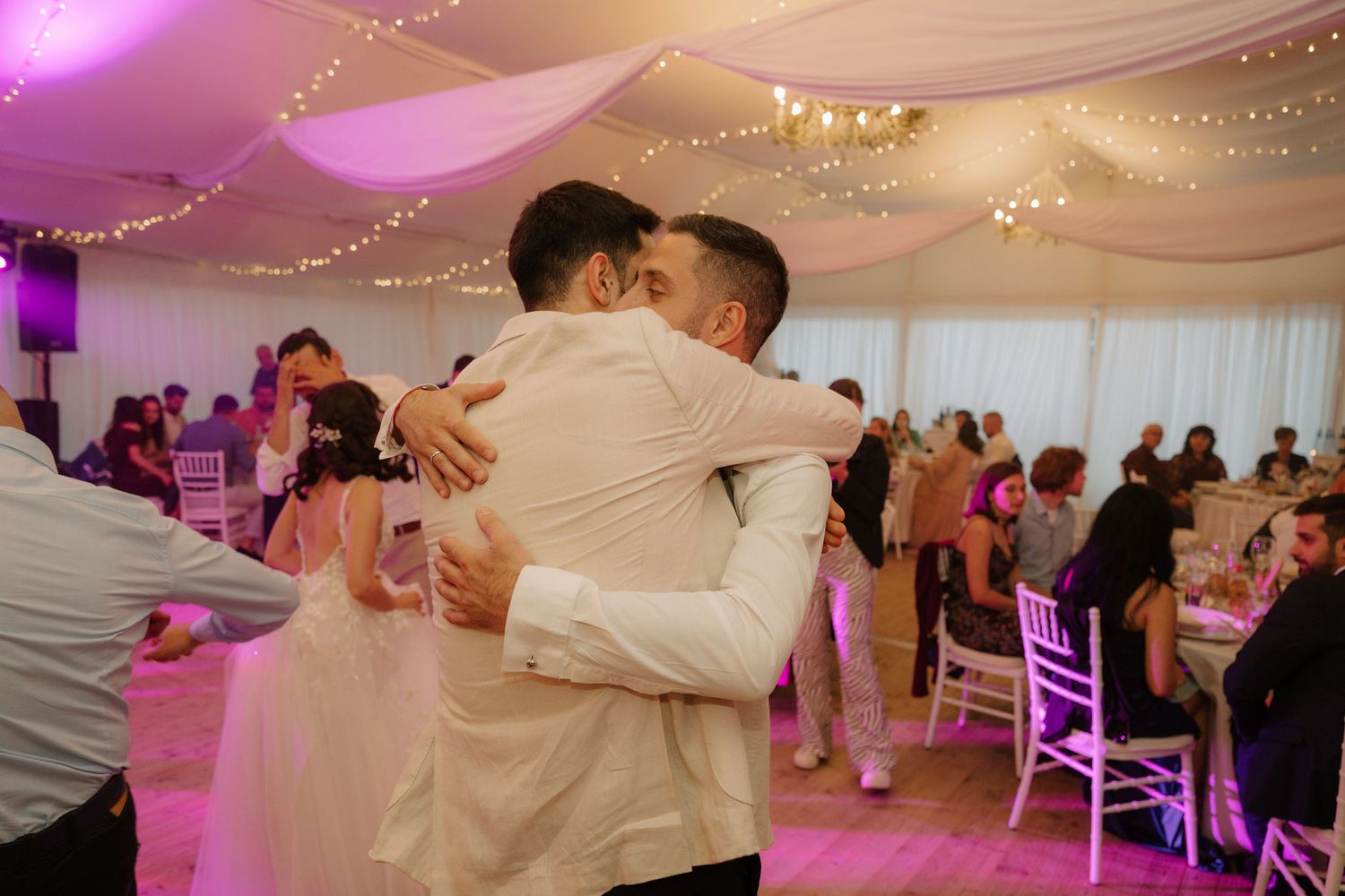 Two grooms share an emotional first dance embrace at their elegant wedding reception with fairy lights.