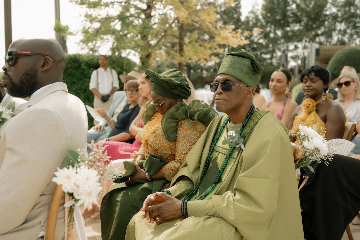Guests in traditional Nigerian attire seated at an outdoor wedding ceremony, wearing green and gold garments.