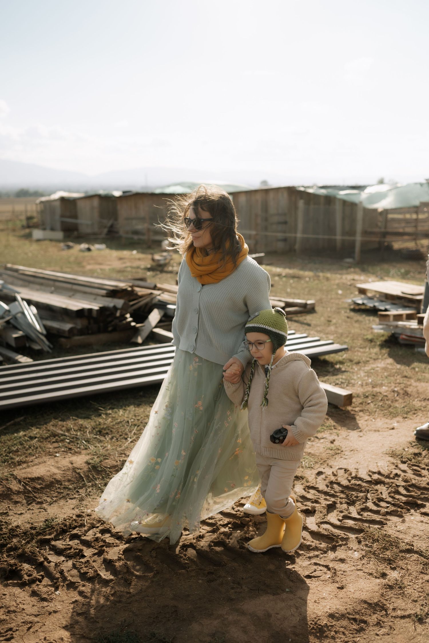 A person in a tulle dress sits on dusty ground while examining debris and materials in a construction area.