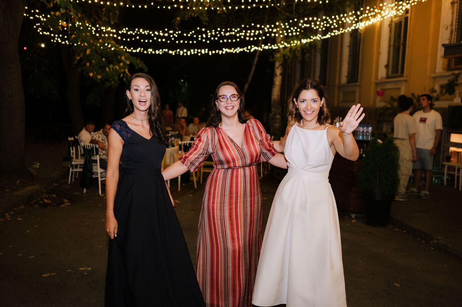 Wedding guests dancing and celebrating under twinkling string lights at an outdoor evening reception.