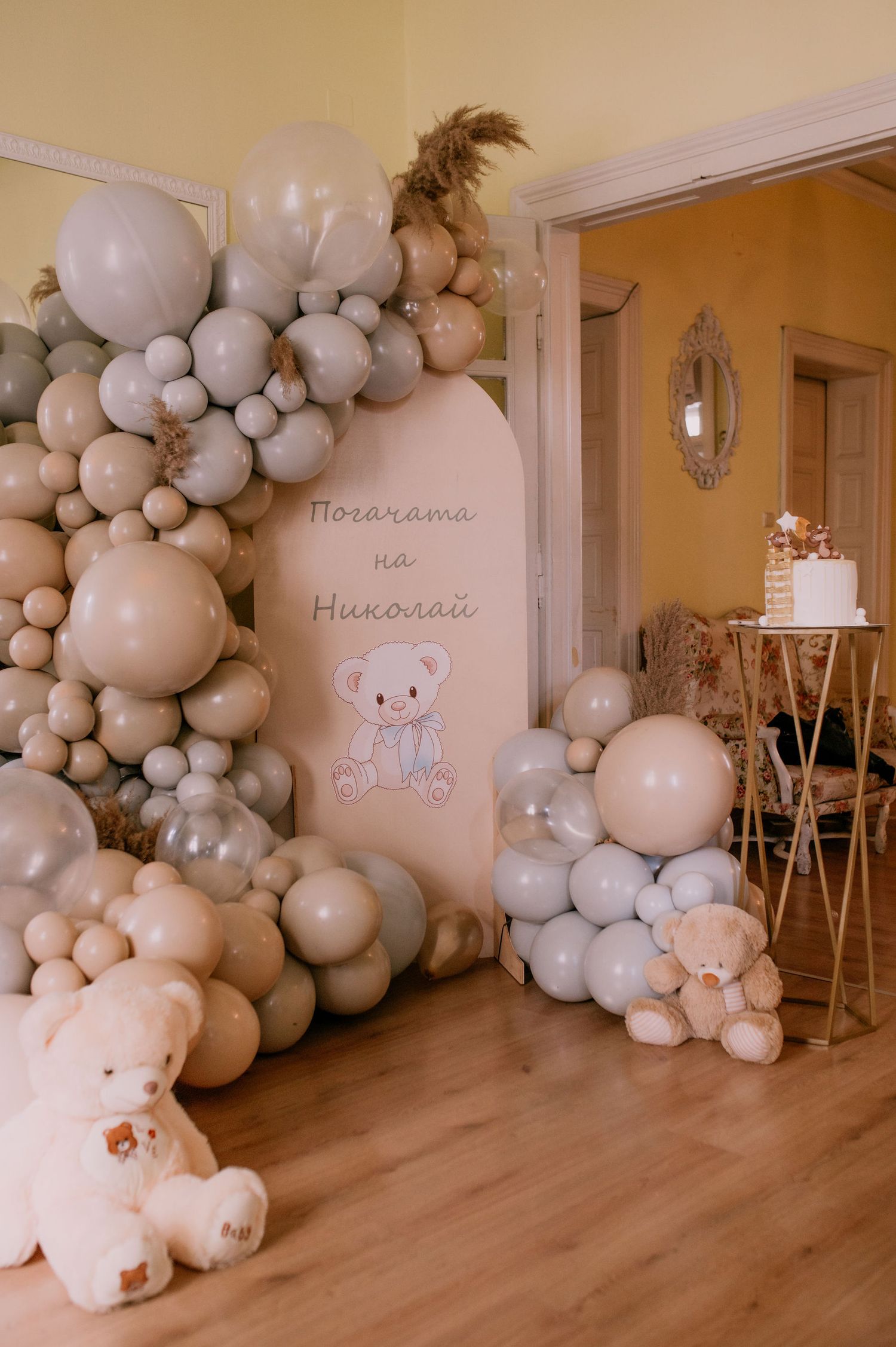 Neutral-toned baby shower setup with grey and white balloon arch, plush toys, and decorative signage.