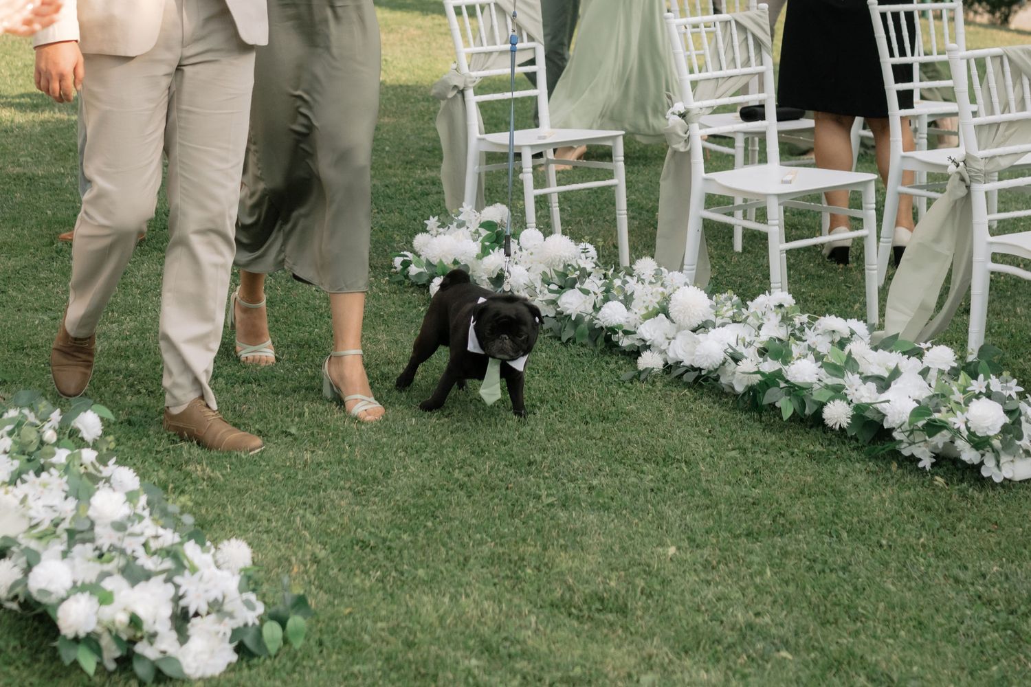 Wedding guests mingle on a manicured lawn with white chairs and floral arrangements at an outdoor ceremony.